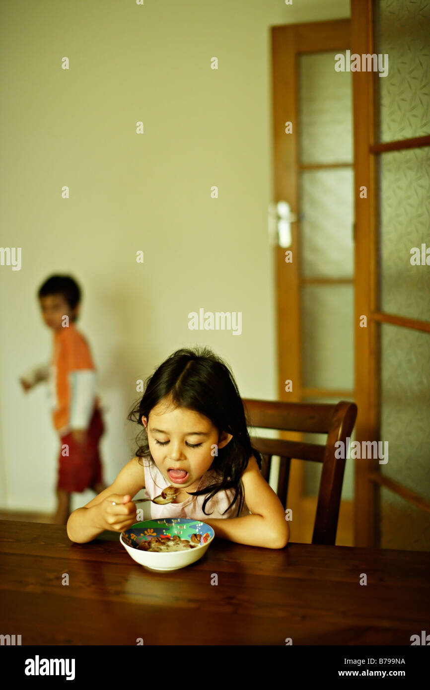 Five year old girl sits at a wooden table and eats a bowl of cereal Stock Photo