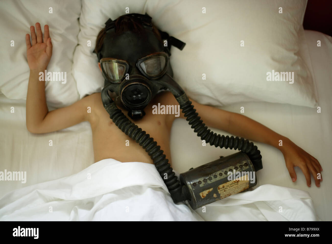 Six year old boy lies in bed wearing gas mask Stock Photo