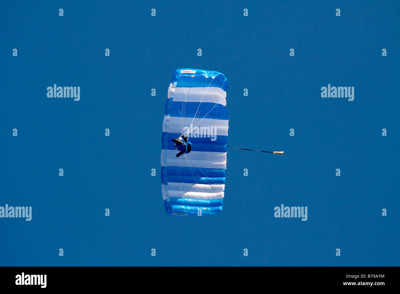 A SKYDIVER HANGS UNDER HIS PARACHUTE AND GLIDES ACROSS THE BLUE SKY Stock Photo