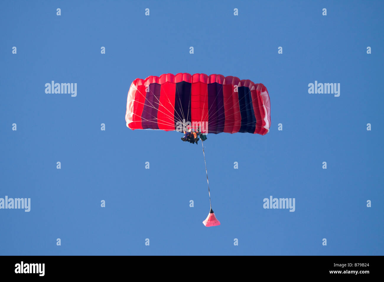 TANDEM SKYDIVE. TANDEM PARACHUTING IN ENGLAND, A RED AND BLUE STRIPED PARACHUTE CARRYING TWO PEOPLE GLIDES ACROSS THE BLUE SKY Stock Photo