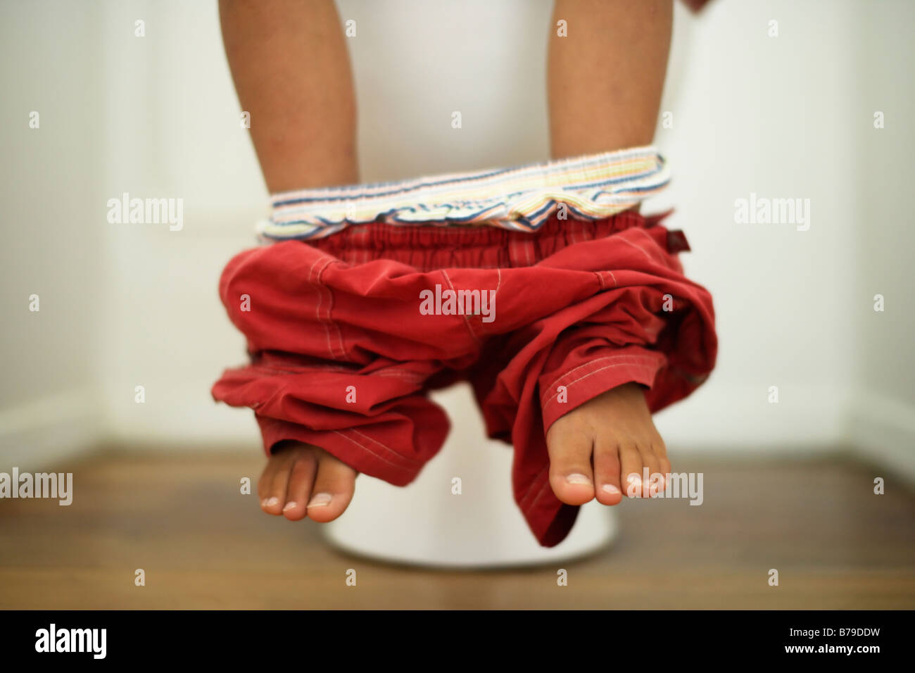Boy sits on toilet with trousers round ankles Stock Photo