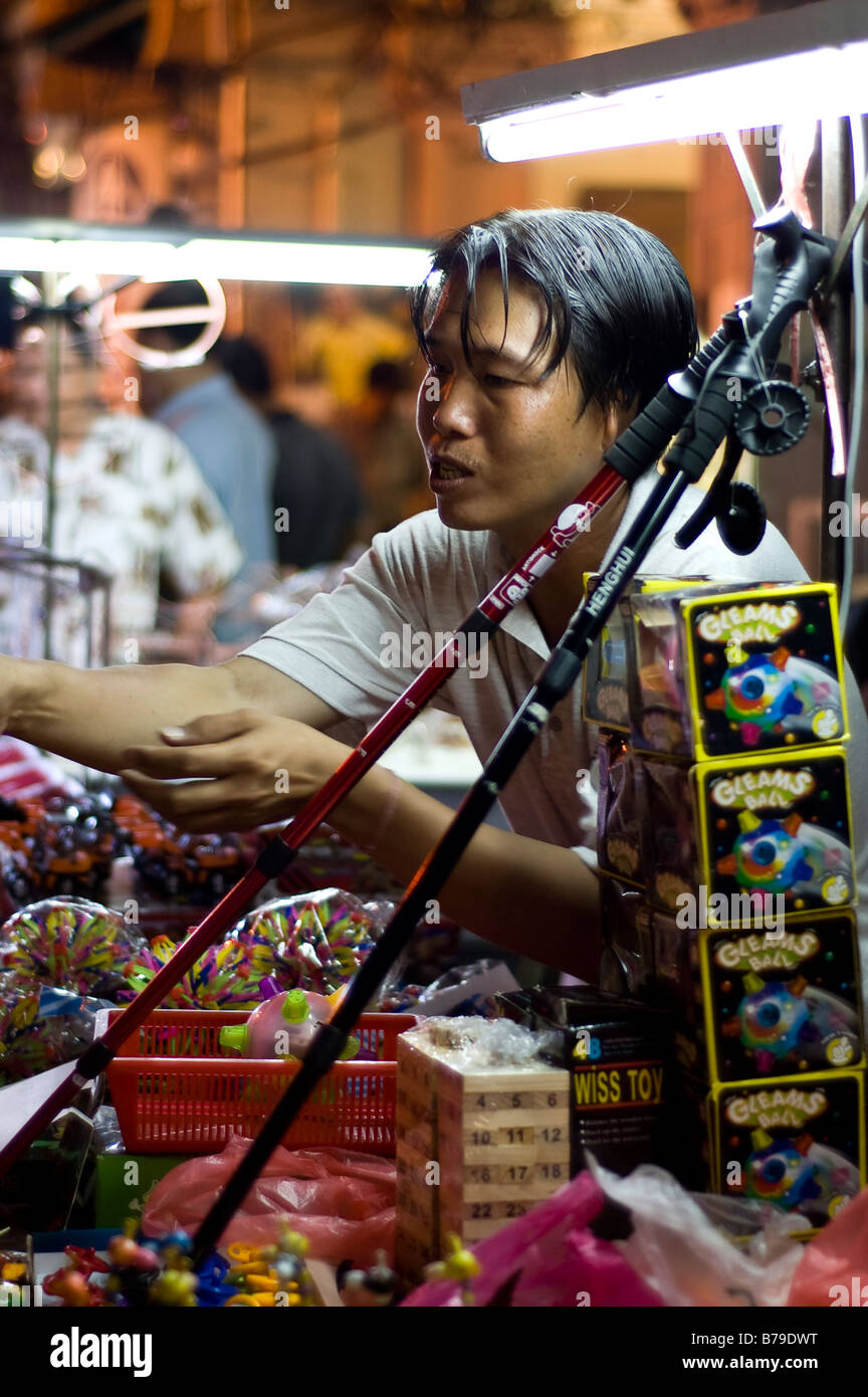 Malaysian man selling toys under neon lights in Melaka street market