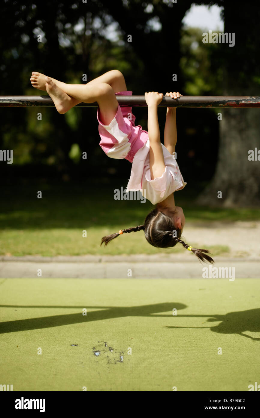 Five year old girl swings her pigtails whilst swinging upside down from a bar Stock Photo