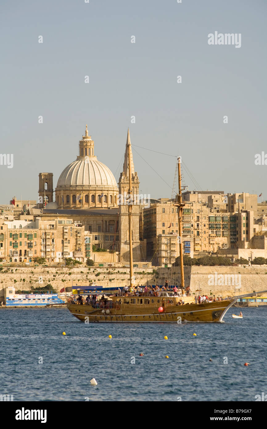 Large yacht cruising in Sliema harbour with buildings in Valletta behind, Valletta, Malta Stock Photo