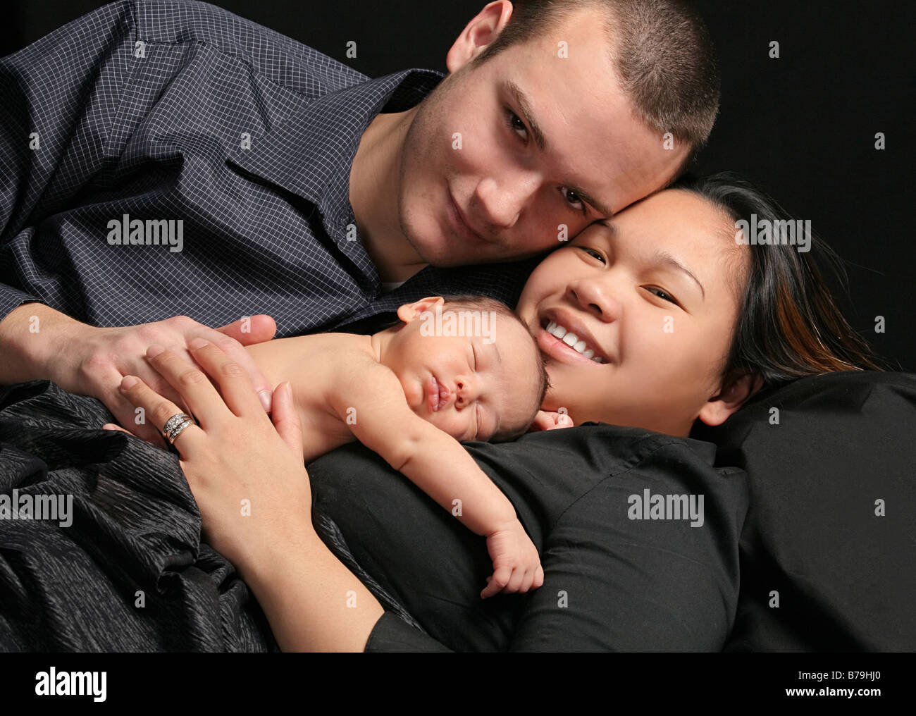young multiracial family in dark clothes lying down with together with sleeping baby Stock Photo
