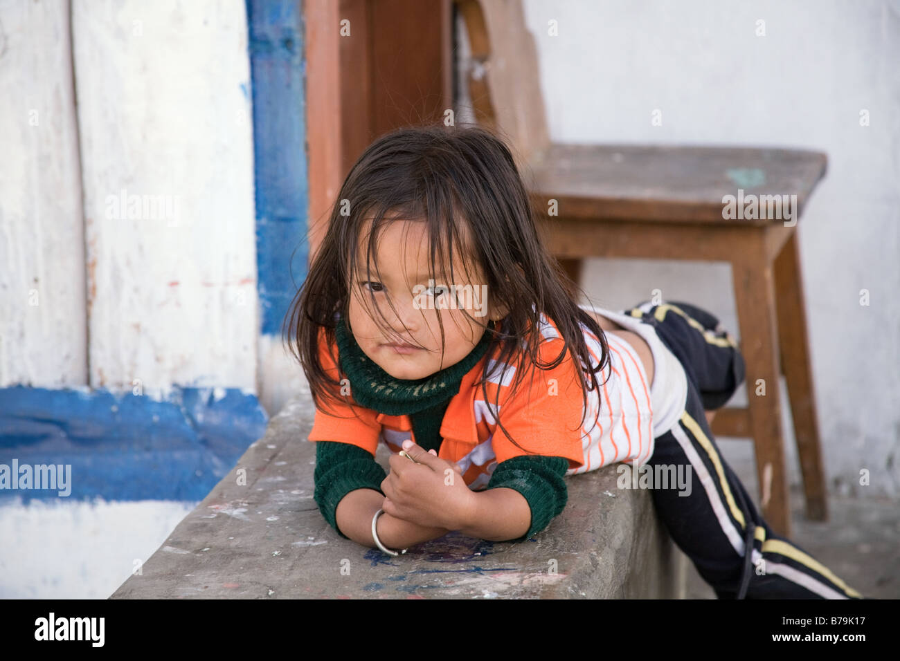A young girl, looking at the camera with an enigmatic smile, lies on a bench in Jakar, central Bhutan Stock Photo