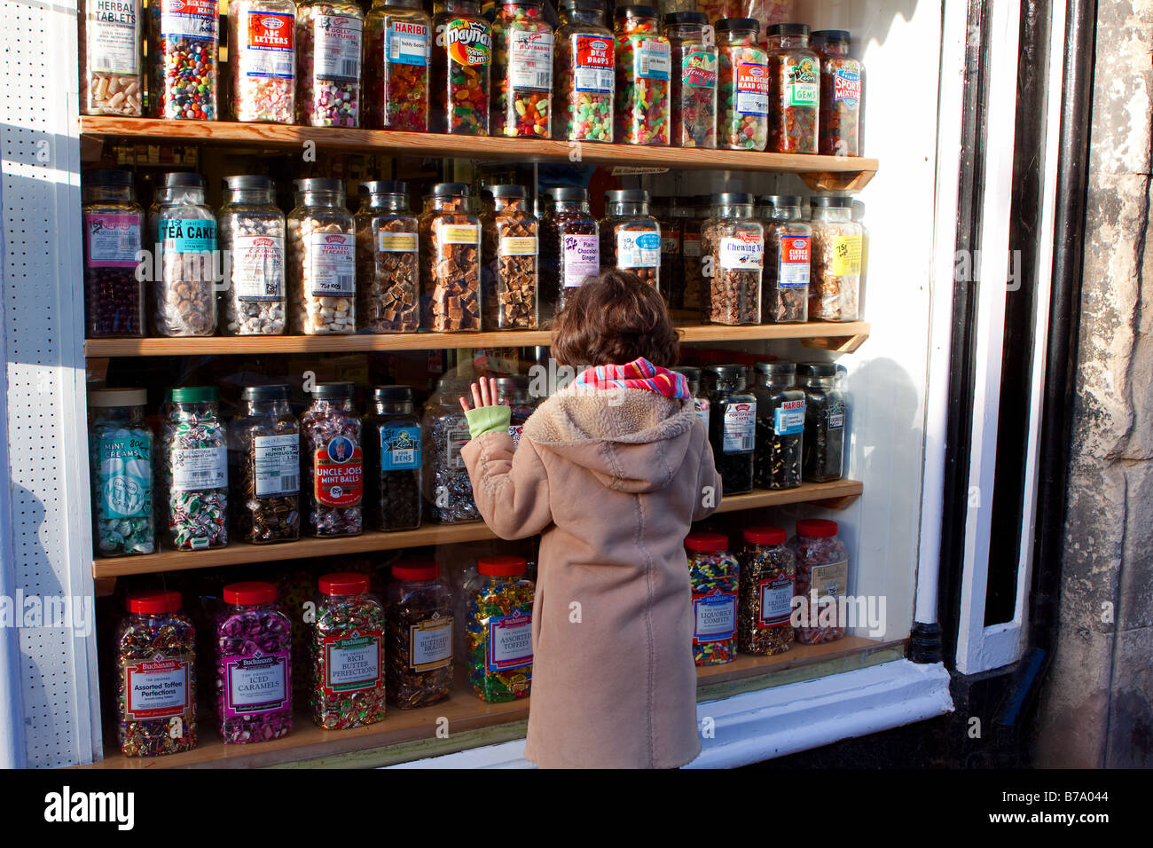 A little girl looks longingly through the shopfront window of a traditional sweet shop in Tenbury Wells Worcestershire Stock Photo