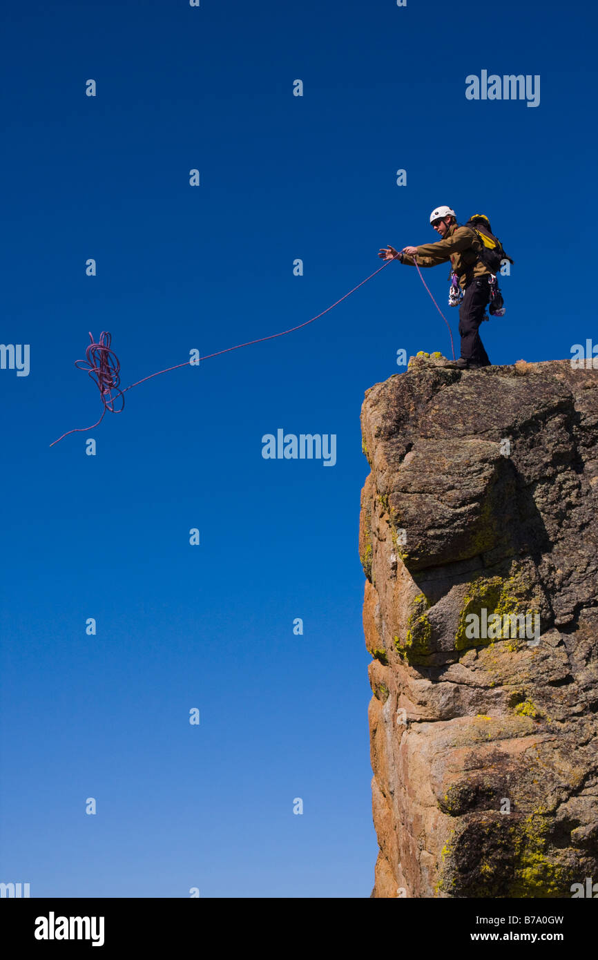 A mountaineer standing on top of a cliff throwing his climbing rope