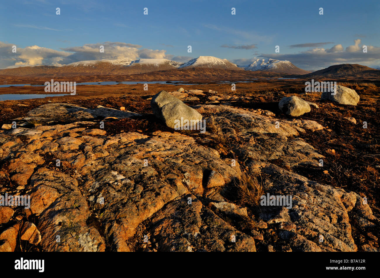 Distant view of snow capped hills across heather moorland with rocks and boulders in foreground Ben Achaladair Rannoch Moor Stock Photo