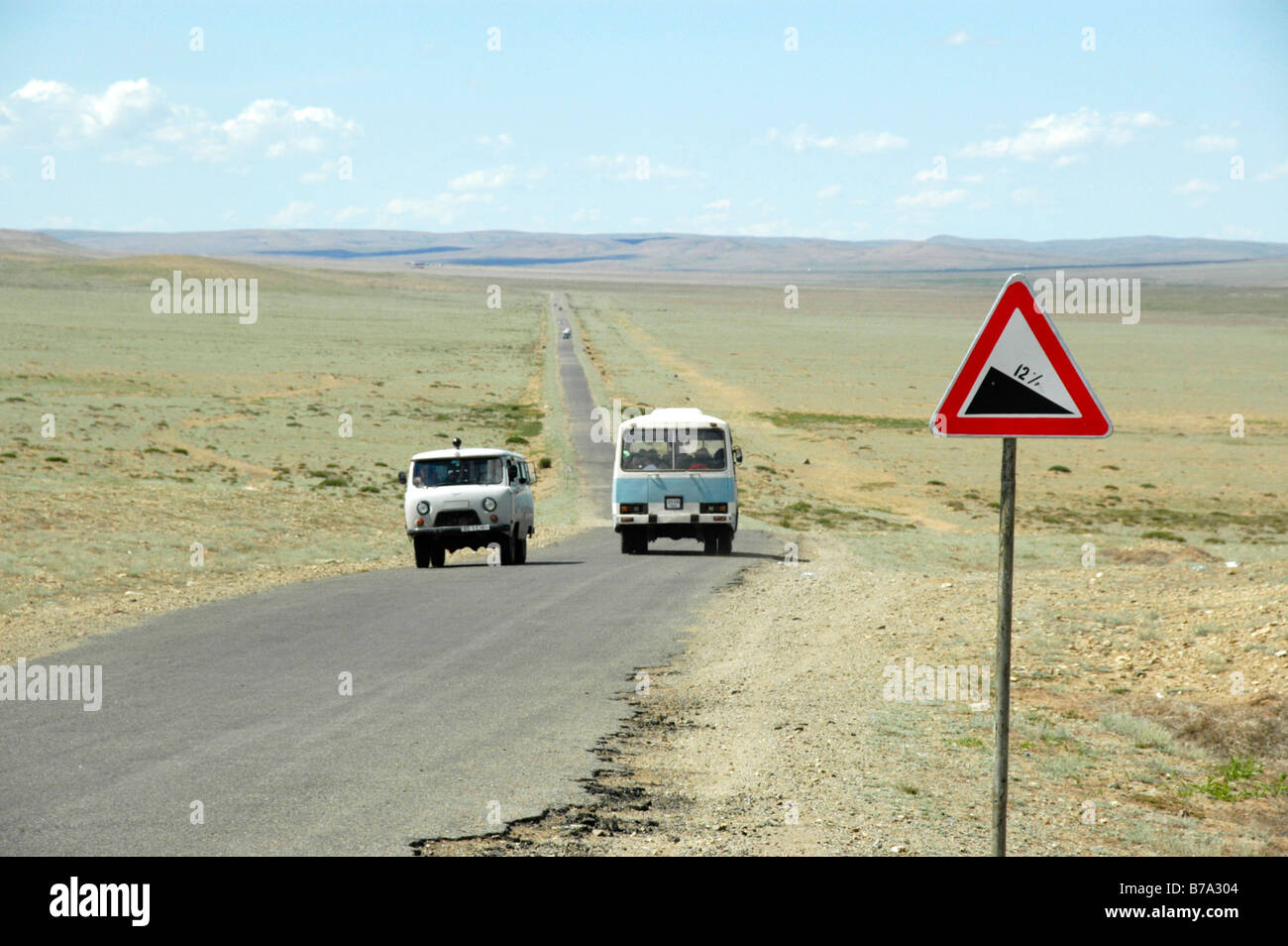 Russian small bus and bus on straight road with road descent sign, wide grassland plain, treeless steppe, Mongolia, Asia Stock Photo