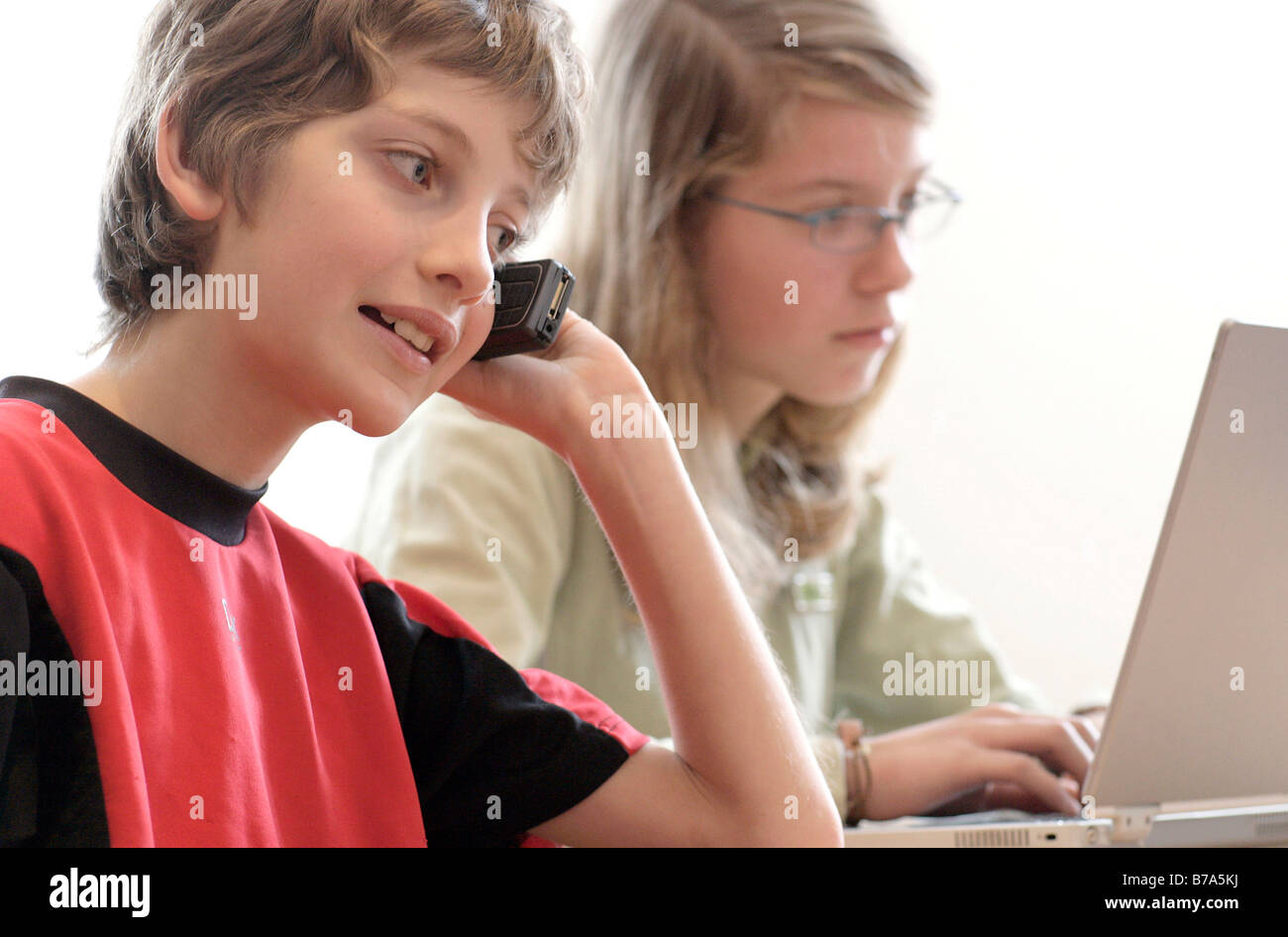 Young 10 year old boy, on cell phone and his 13 year old sister on a laptop Stock Photo