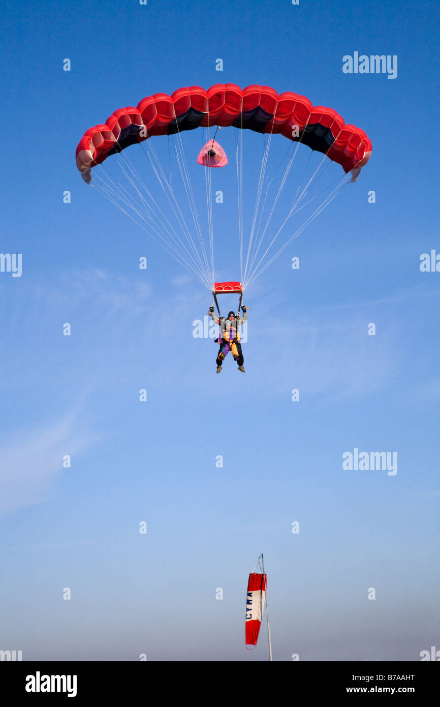 TANDEM PARACHUTING IN ENGLAND. TANDEM JUMPERS UNDER A RED PARACHUTE PREPARE FOR LANDING AS THEY PASS A LIMP WINDSOCK Stock Photo