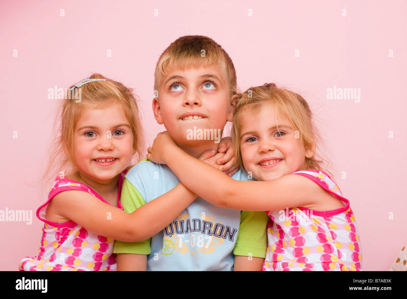 3 year old twin girls embracing a seven year old boy Stock Photo