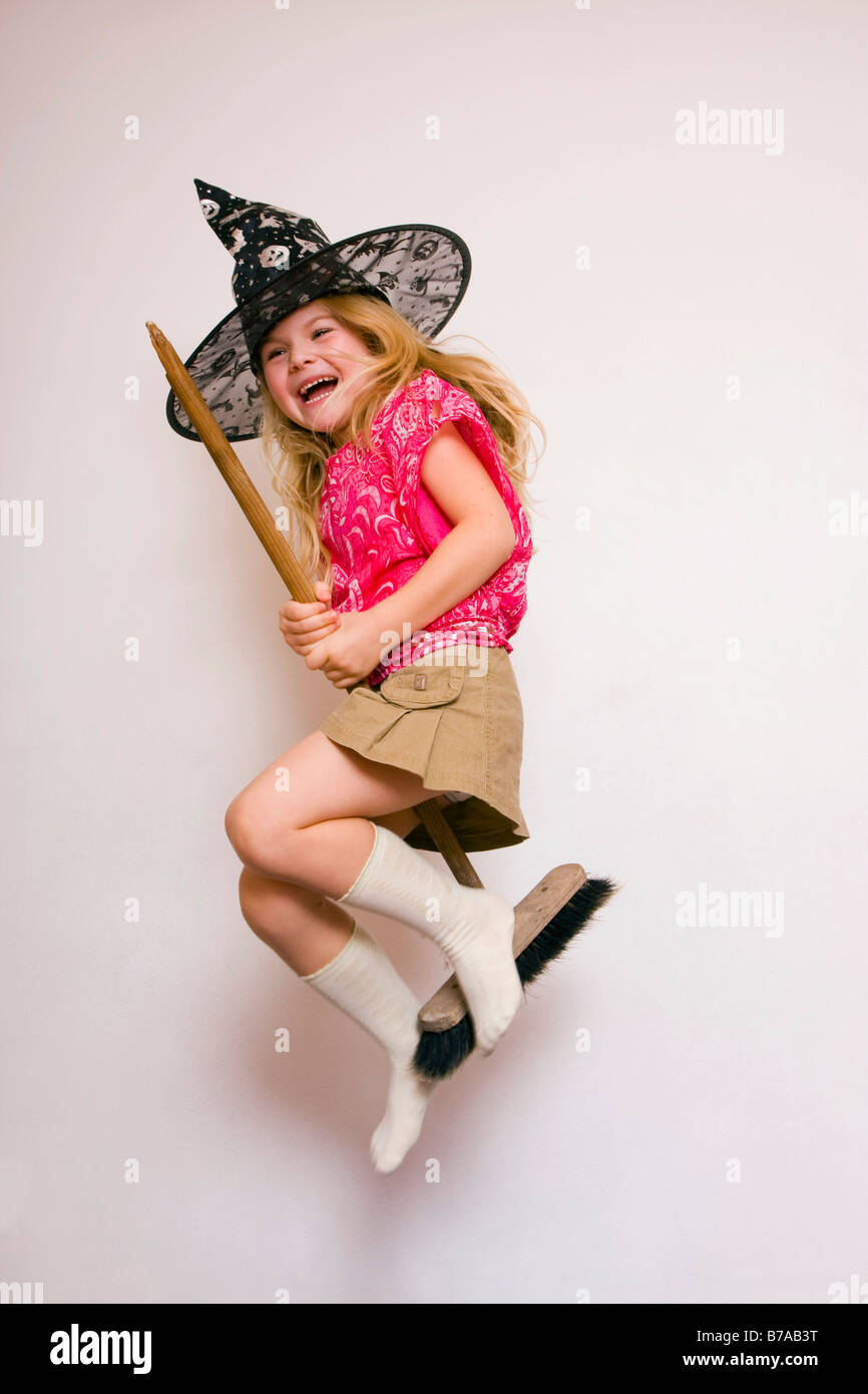 5 year old girl on a broomstick wearing a witches hat, against neutral background Stock Photo
