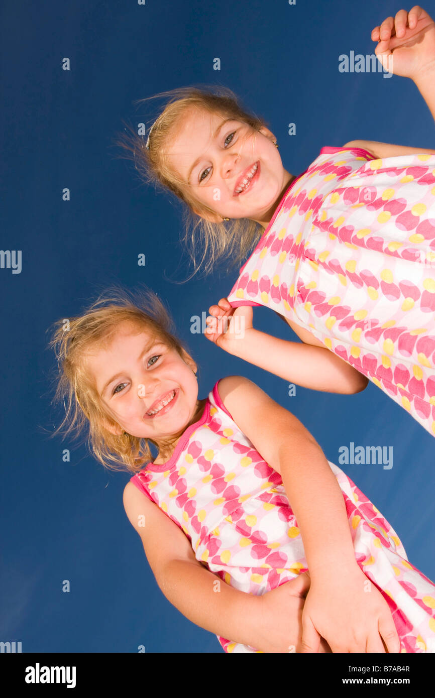 3 year old smiling twin girls against blue sky Stock Photo