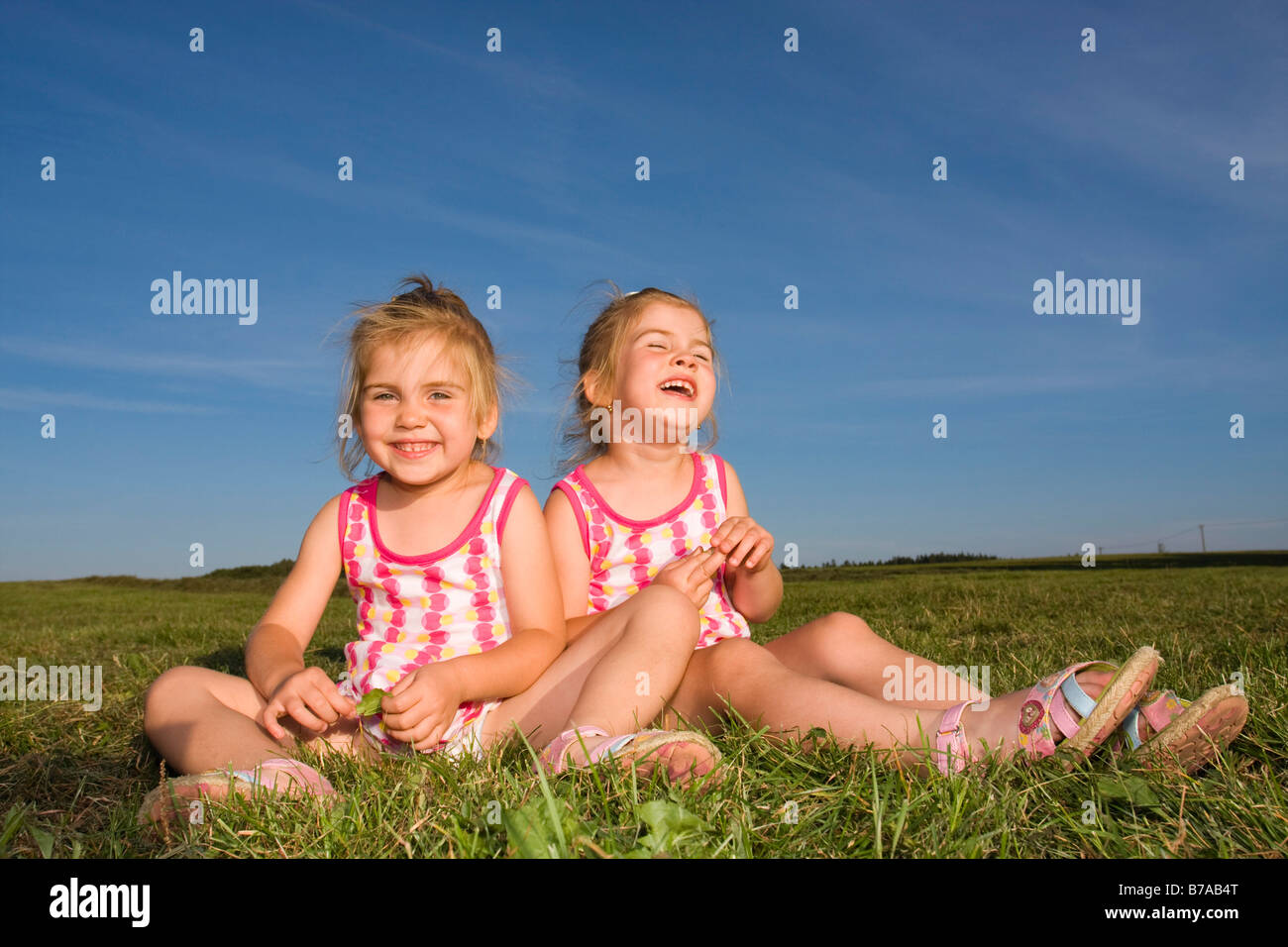 3 year old smiling twin girls sitting on grass in summer Stock Photo