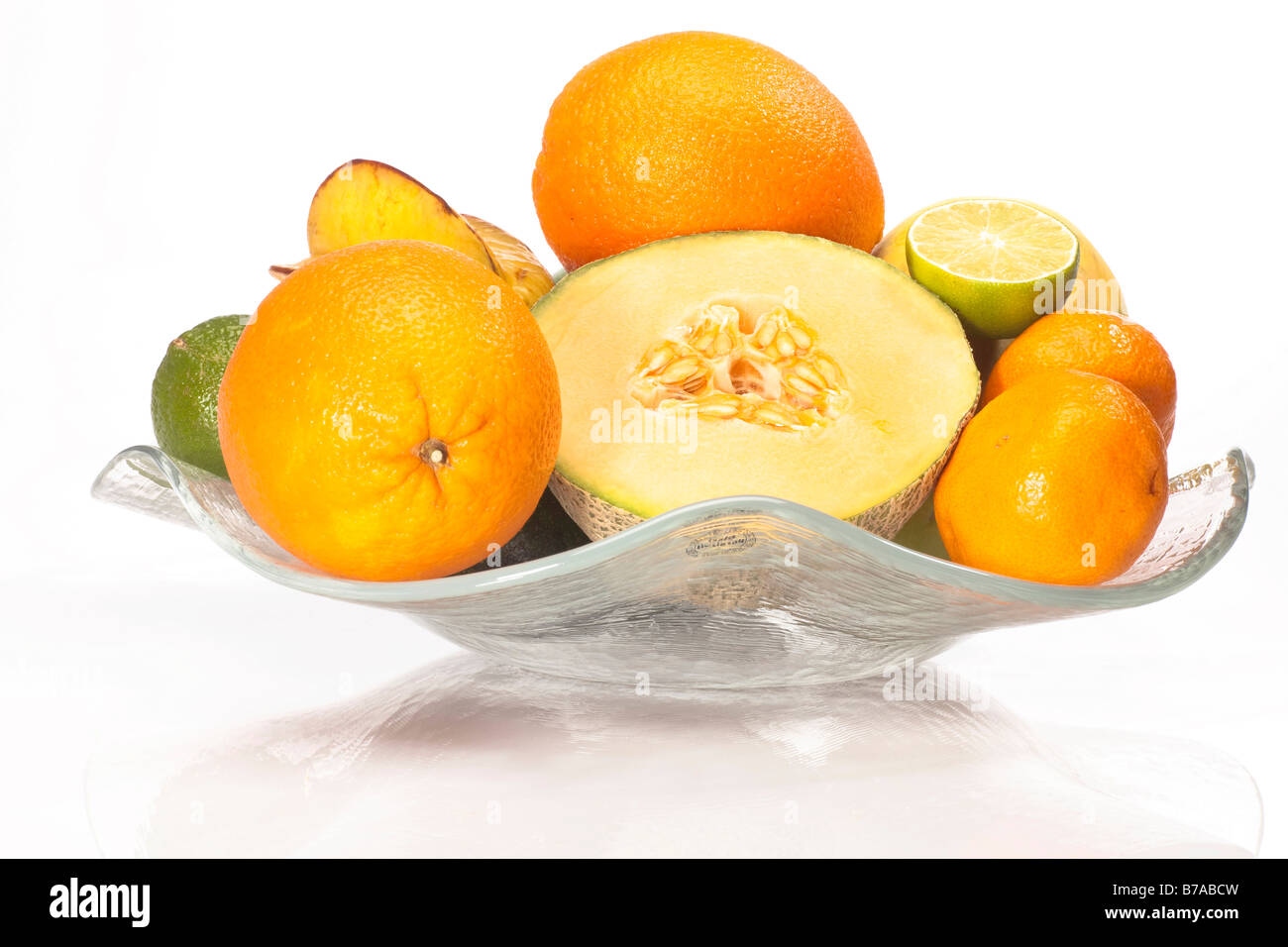 Sliced honeydew melon, oranges, mandarins, limes and star fruit in a glass bowl Stock Photo