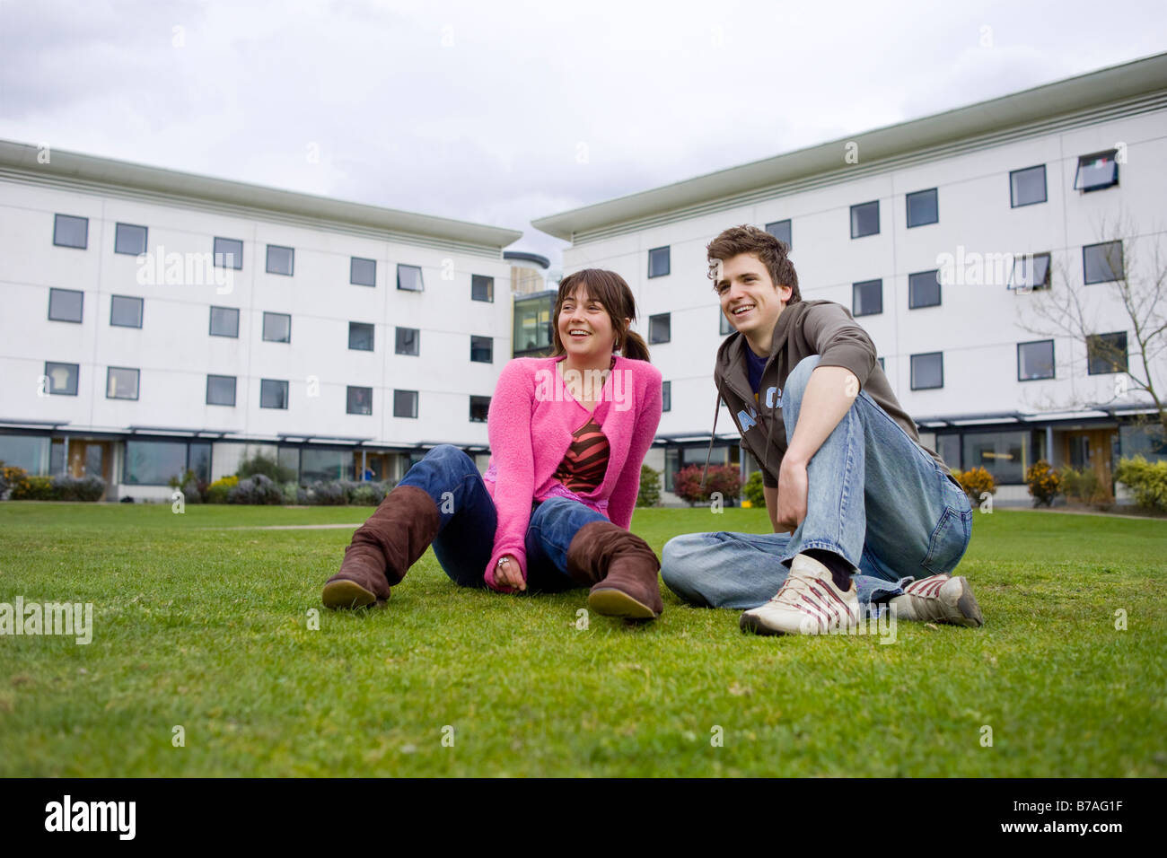 Two students at breaktime having a friendly chat on the grass outside the university building Stock Photo