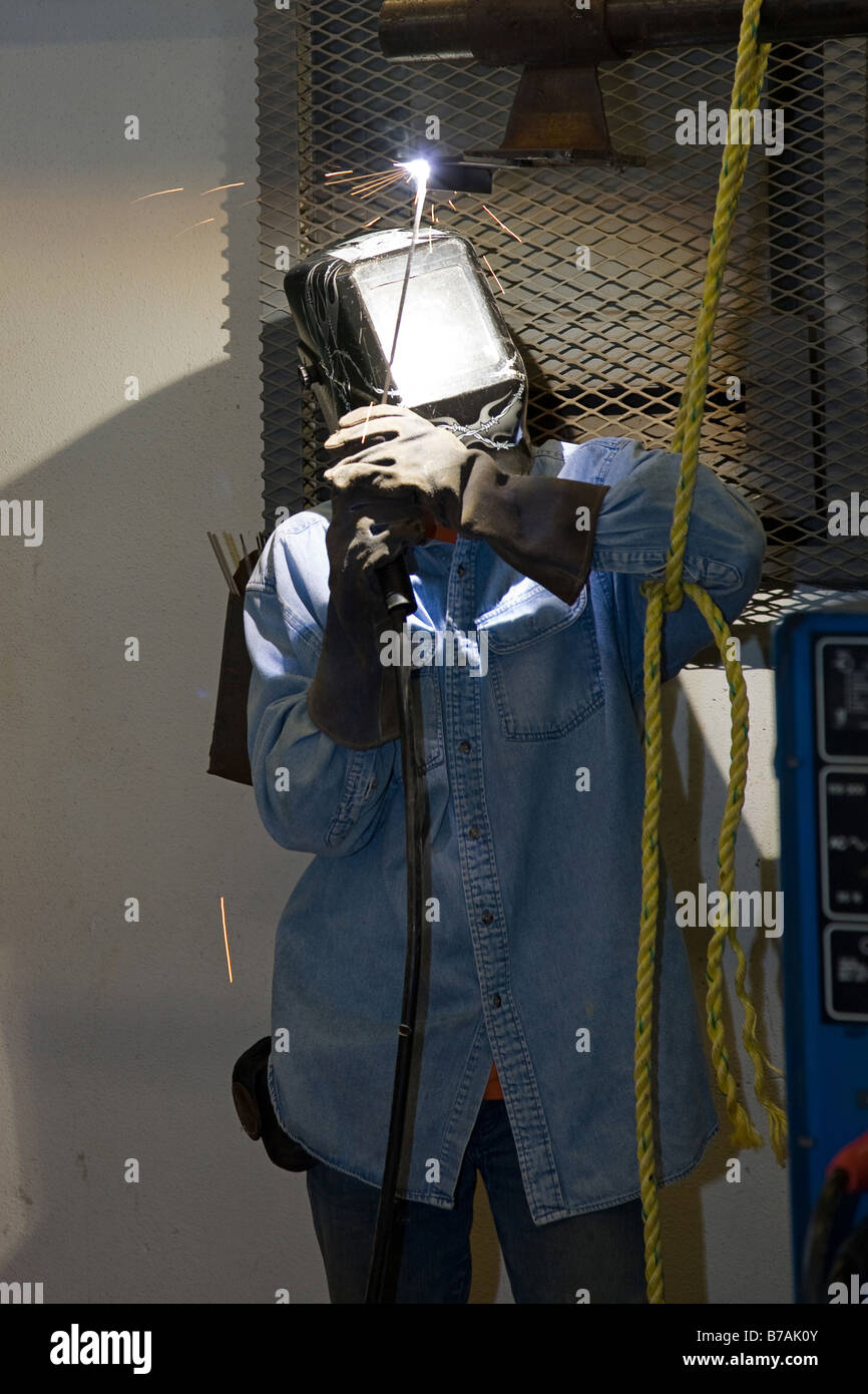 Welder properly outfitted in safety gear welding metal over his head