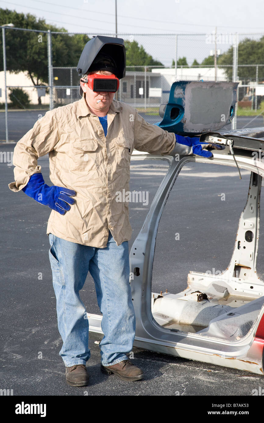 Factory worker taking a smoke break leaning against a disassembled automobile Stock Photo
