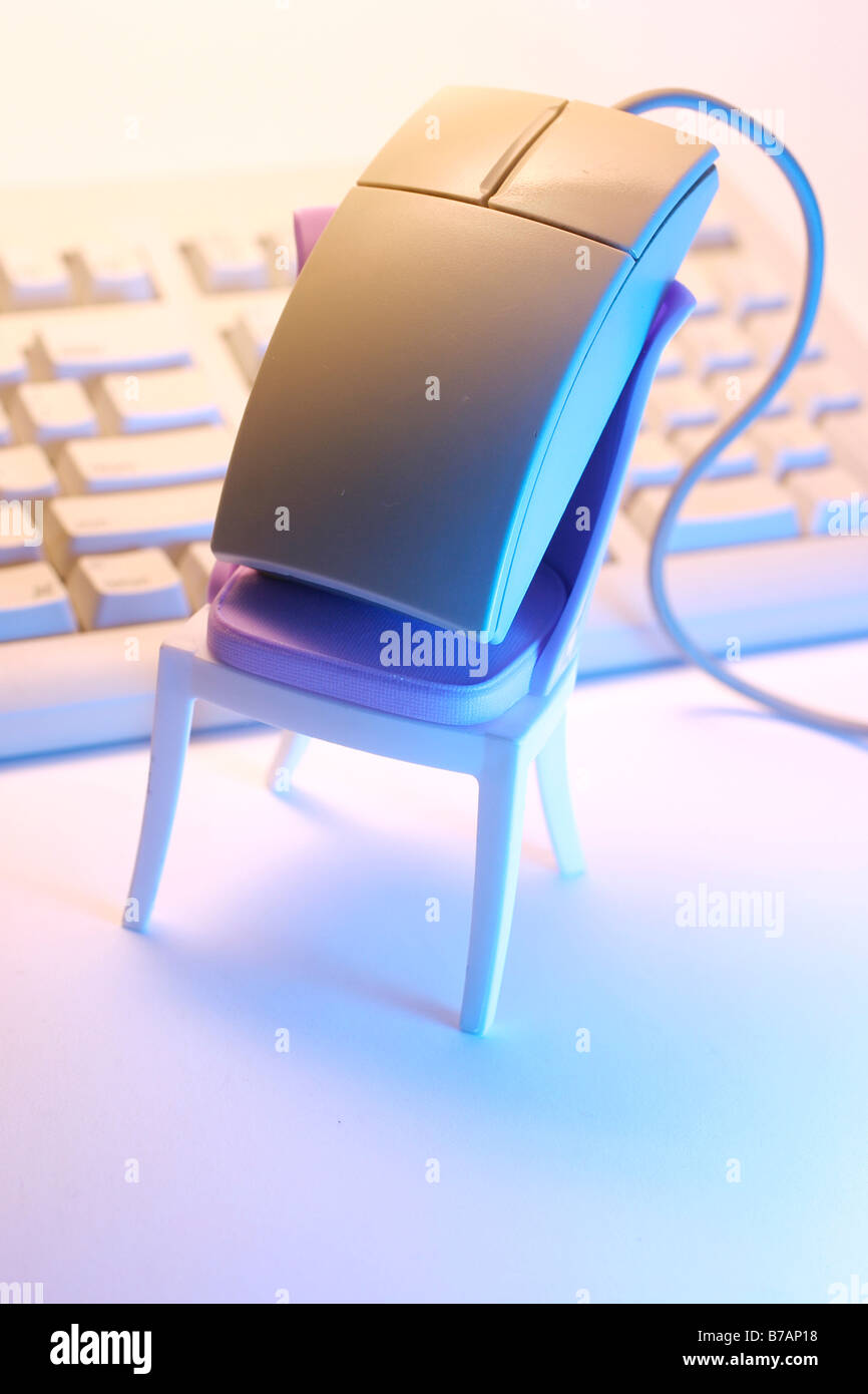 Computer mouse perched on a mini chair, keyboard Stock Photo