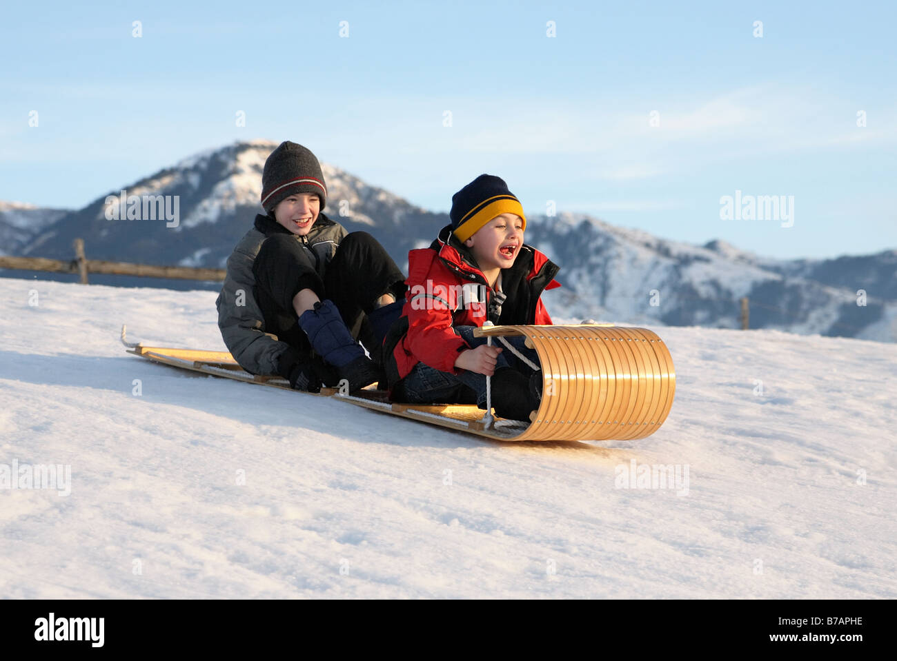 two boys sledding down a hill on a toboggan with excited expressions Stock Photo
