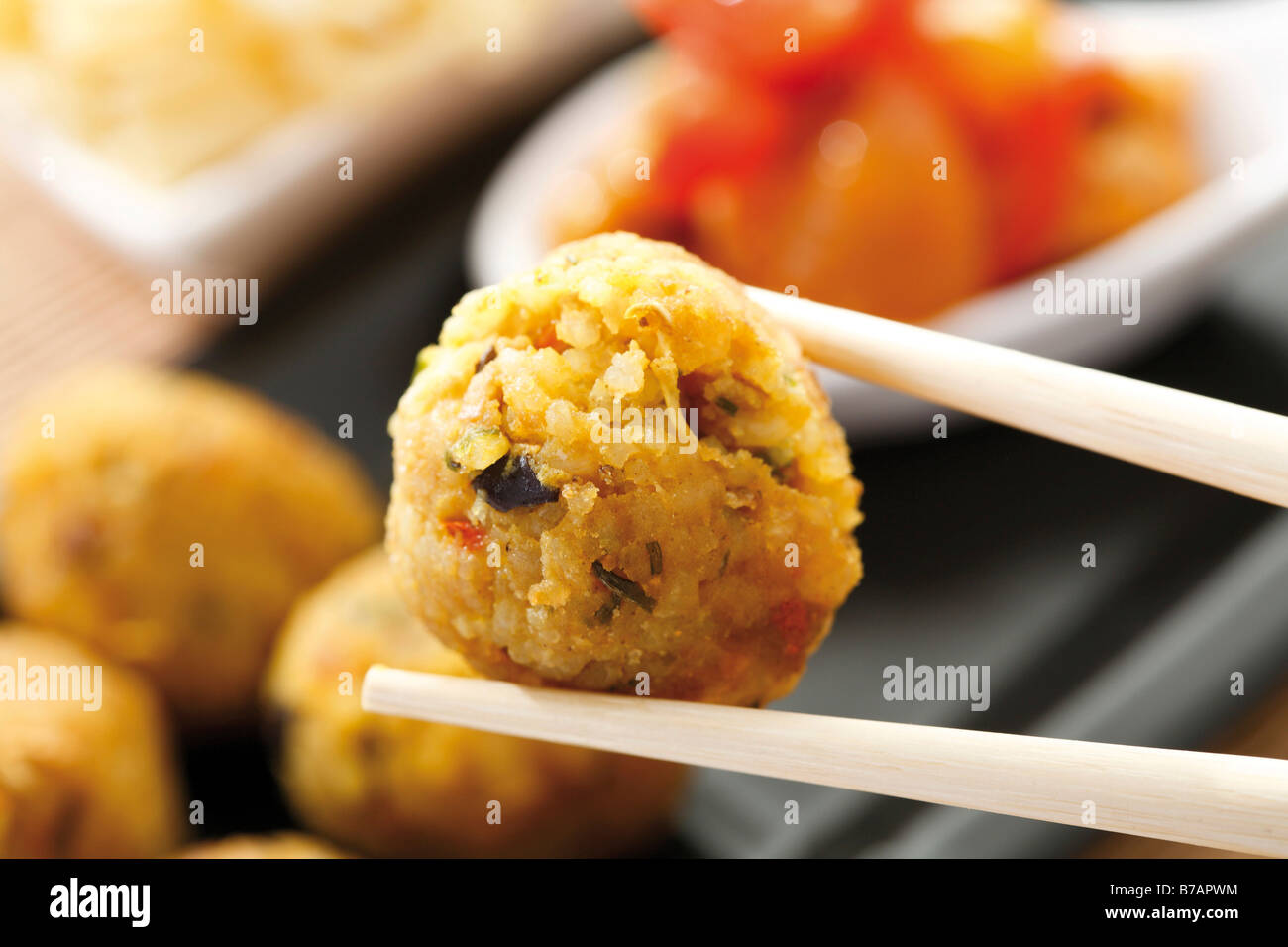 Asian, curry-flavoured ball of rice held with chopsticks, chicken breast with red peppers and noodles Stock Photo