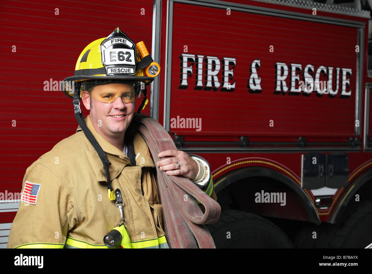 horizontal portrait of a happy fireman standing in front of fire engine in uniform holding a fire hose Stock Photo