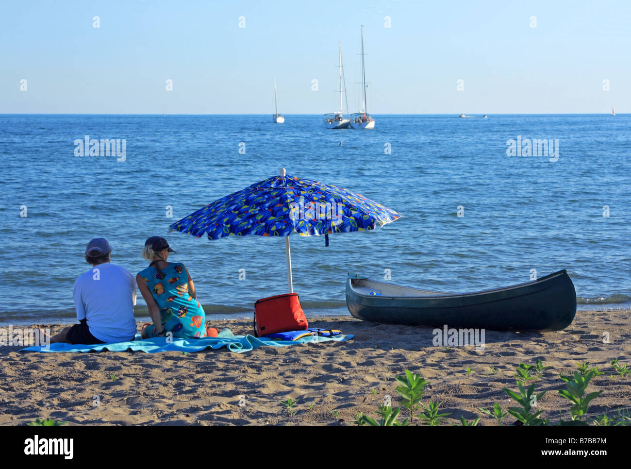 Couple sitting on sandy beach of Wards Island watching blue water of Lake Ontario Stock Photo
