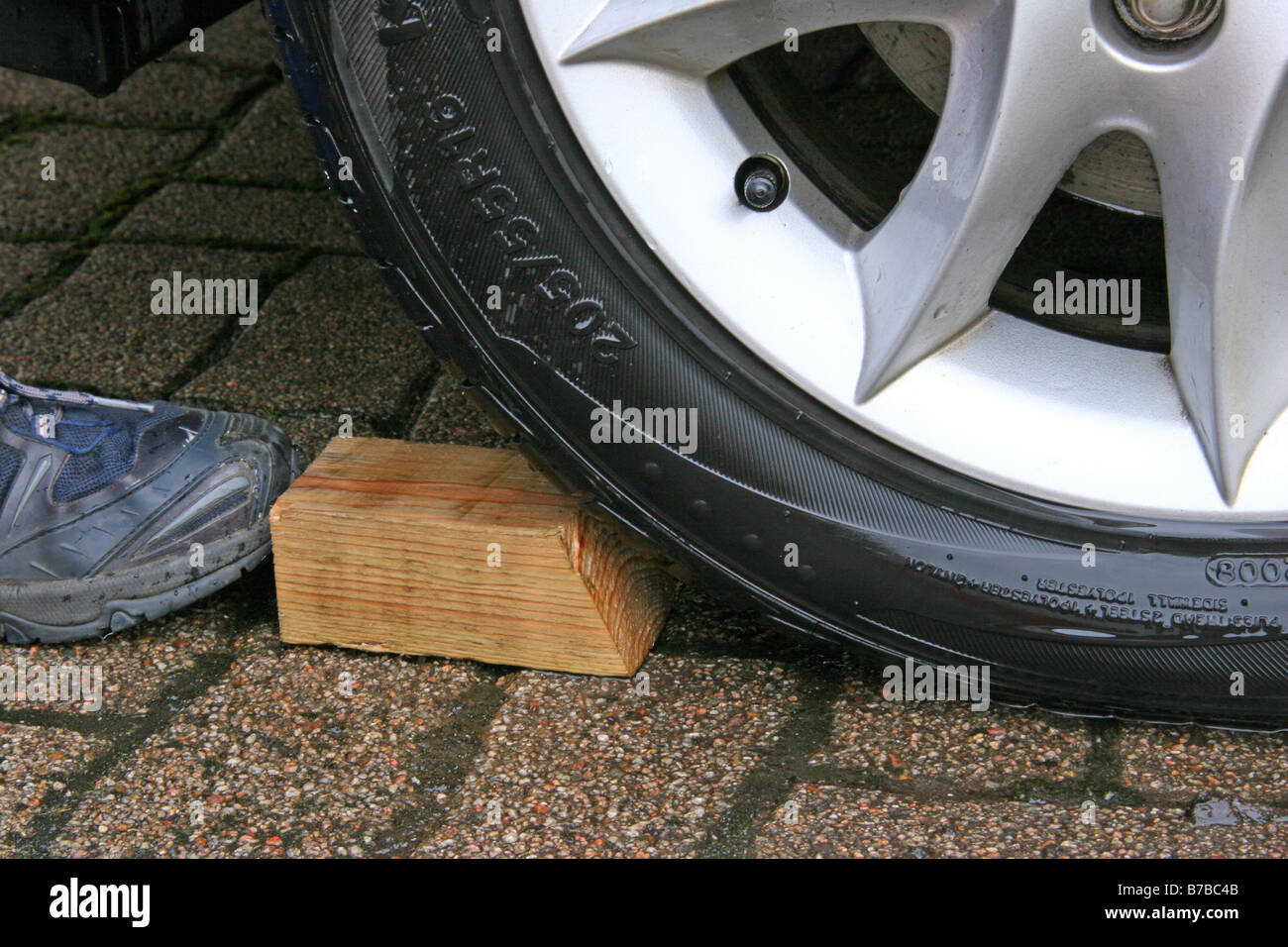 Block of wood wedged on car tyre to prevent car rolling Stock Photo