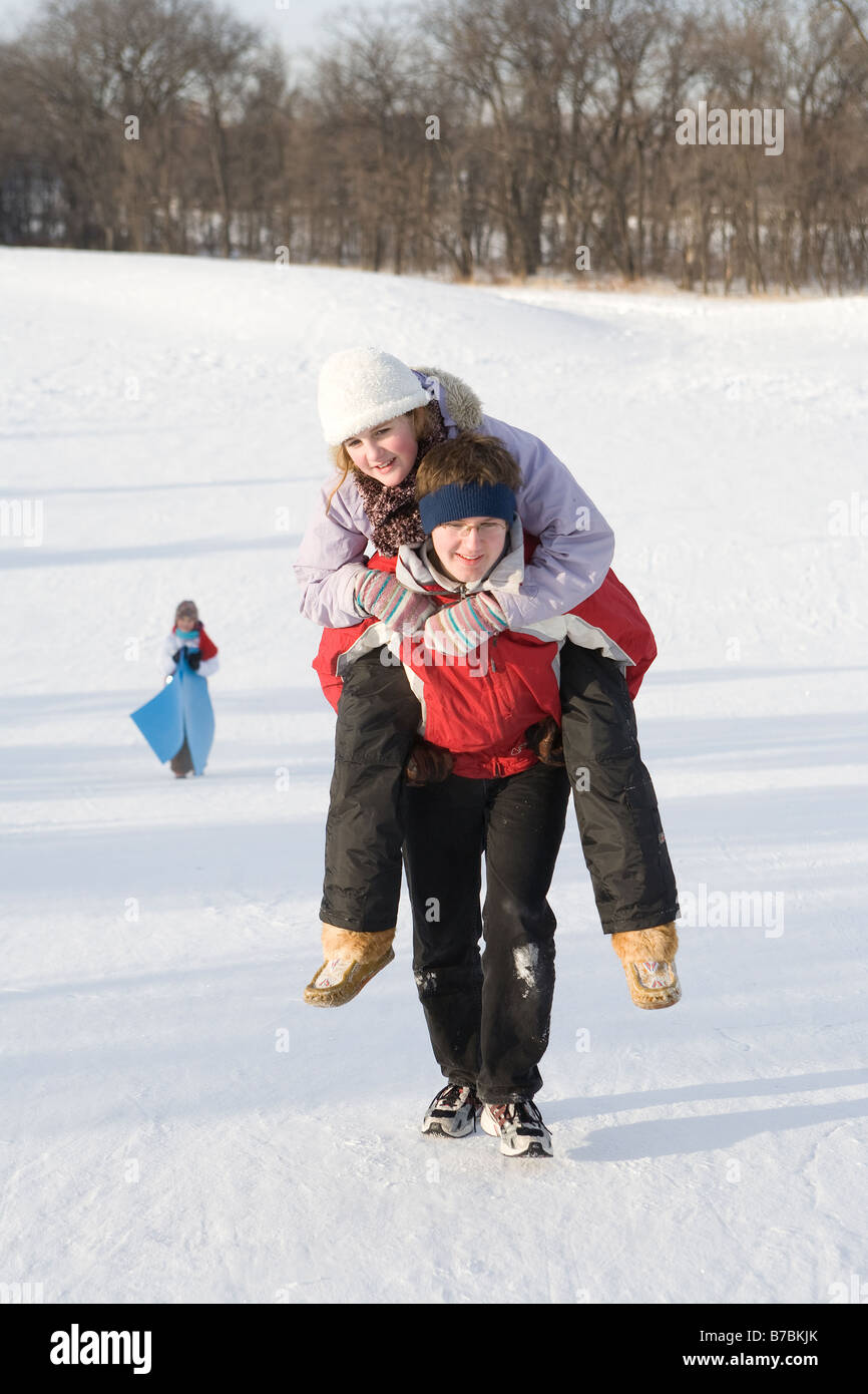 15 year old piggy-backs 13 year old girl up hill, outdoor winter, Winnipeg, Canada Stock Photo