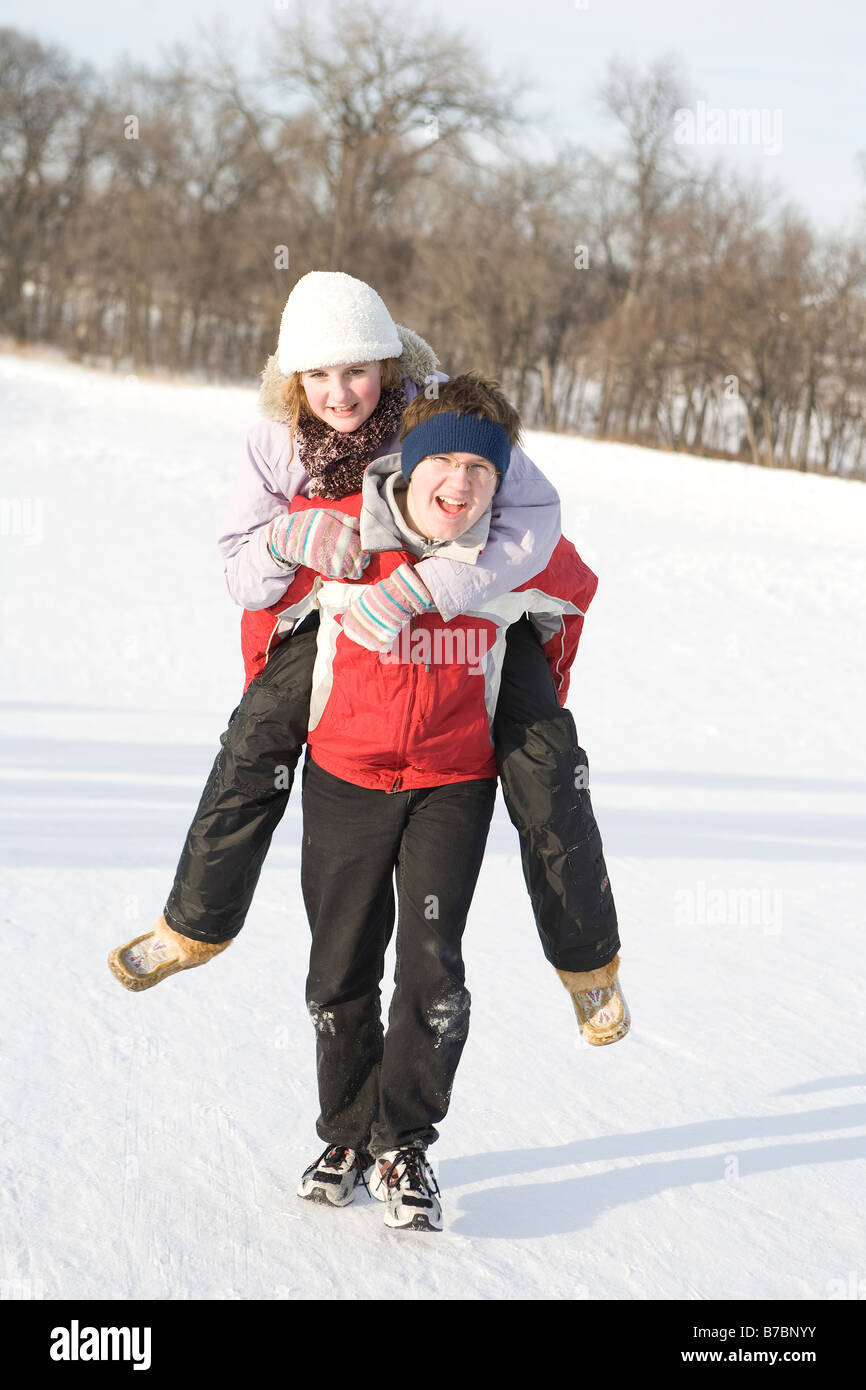 15 year old piggy-backs 13 year old girl up hill, outdoor winter, Winnipeg, Canada Stock Photo