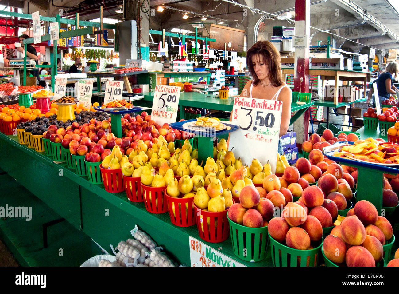 A woman shops for summer fruit at the outdoor Marche Jean Talon in French speaking note signs Montreal Quebec Stock Photo