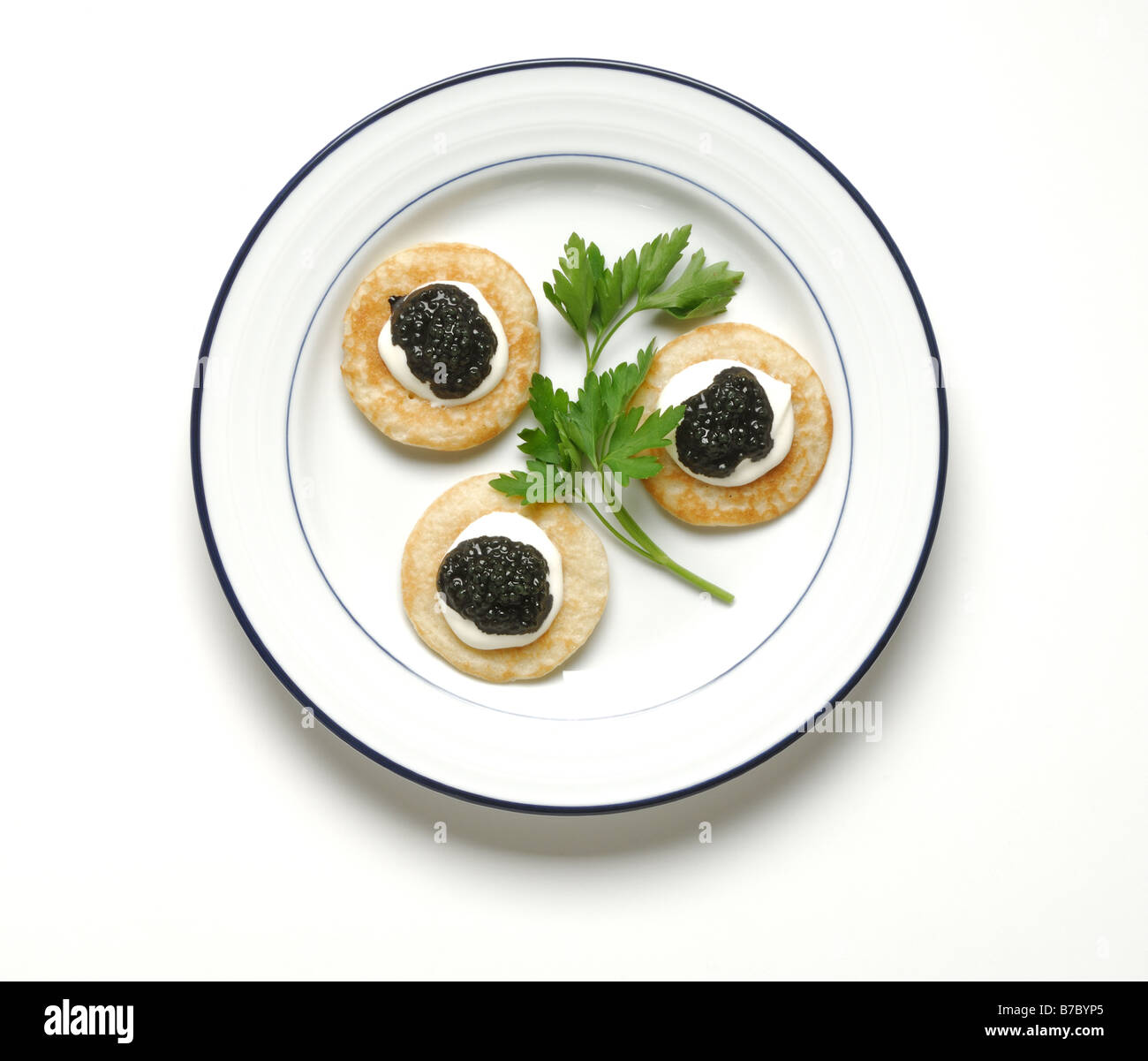 Three crackers with black caviar, green garnish on a round white dinner plate Stock Photo