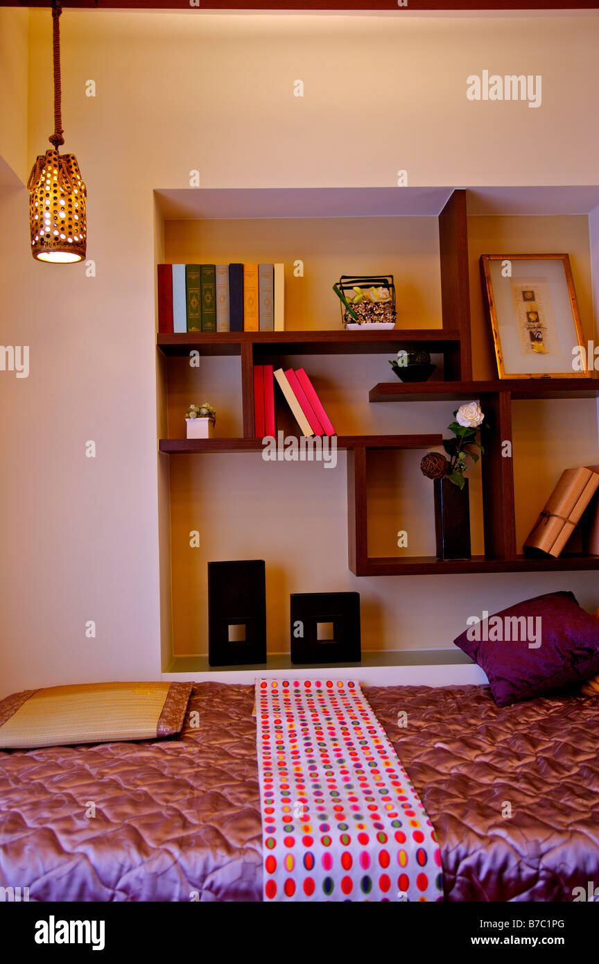 Colorful bed beside shelves with ornaments and books on display Stock