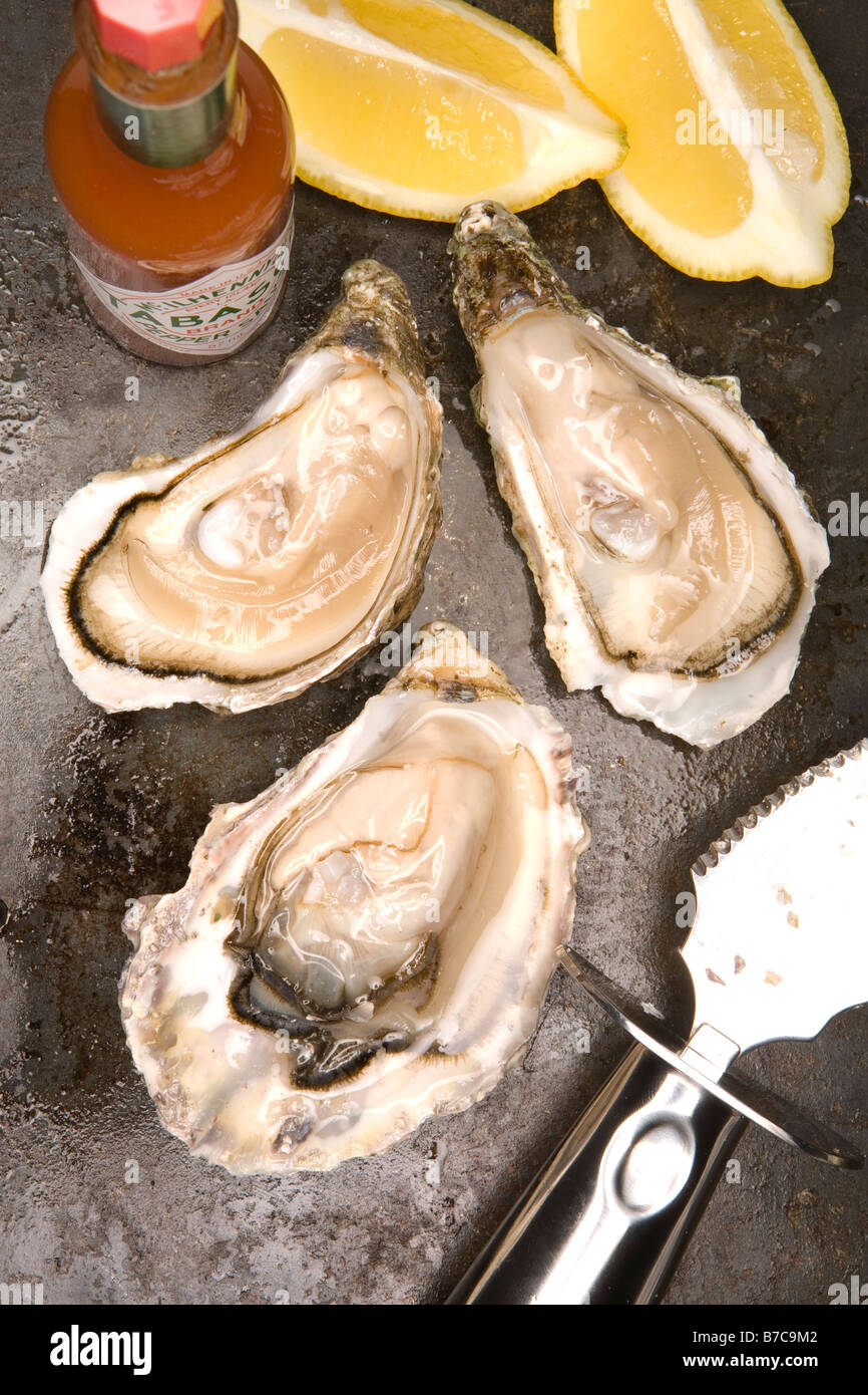 three fresh oysters slices of lemon tabasco sauce oyster knife Stock Photo