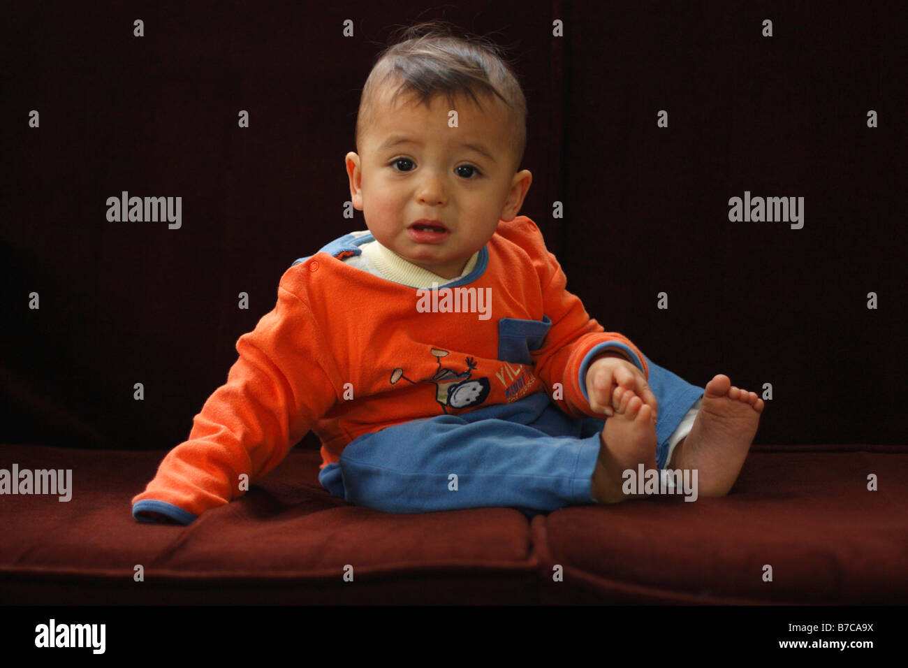 Upset one year old boy sitting on a couch. Stock Photo