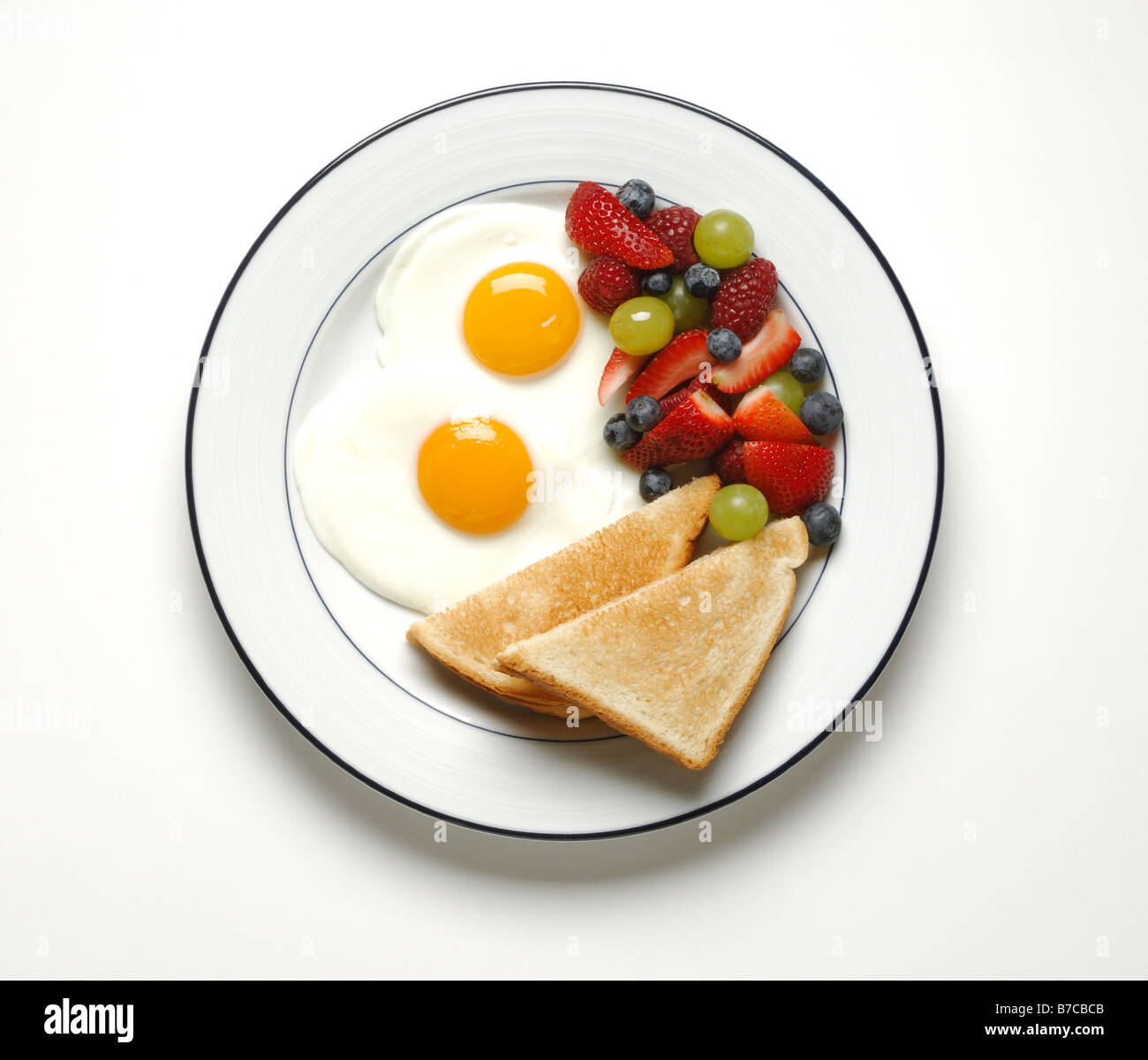 A breakfast serving of fried eggs, toast and mixed fruits Stock Photo
