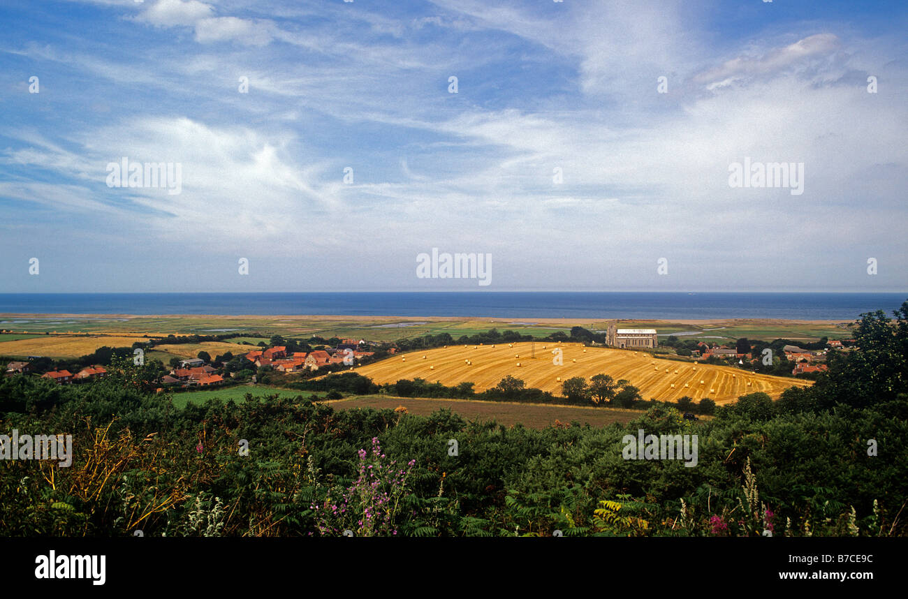 summer fields overlooking St Nicholas Church and the salt marshes protected by shingle banks on the North Norfolk coast Stock Photo