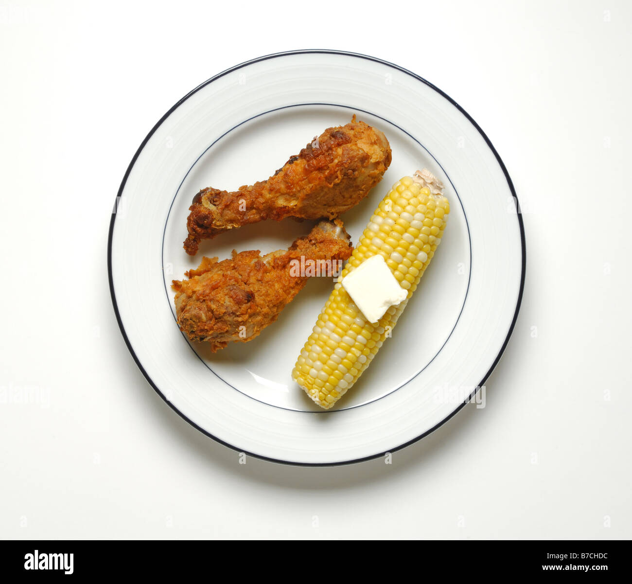Two pieces of fried chicken and corn on the cob with butter on a round white dinner plate. Stock Photo