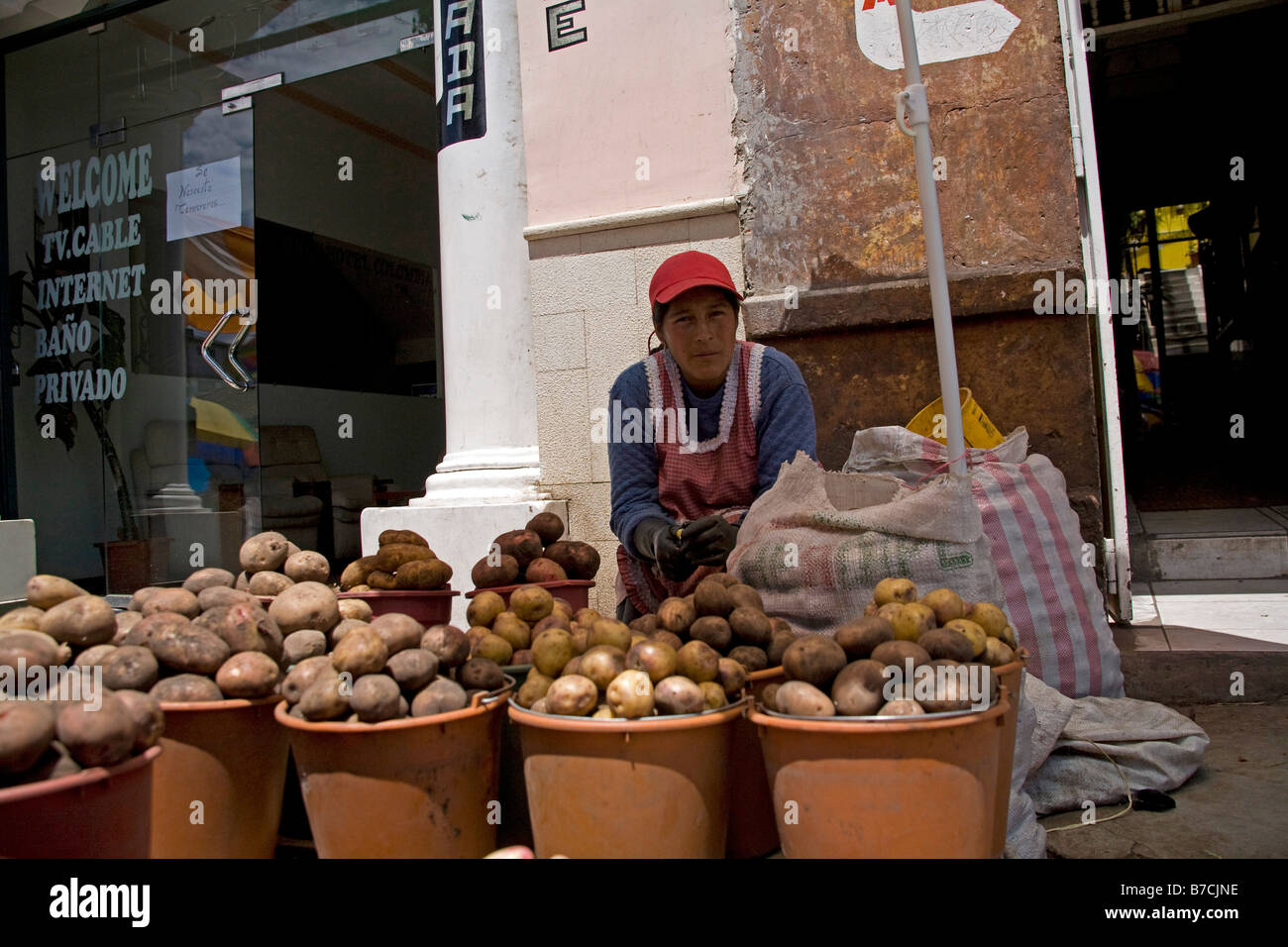 Outdoors Market trader selling potatoes, Wearing red hat in Ecuador