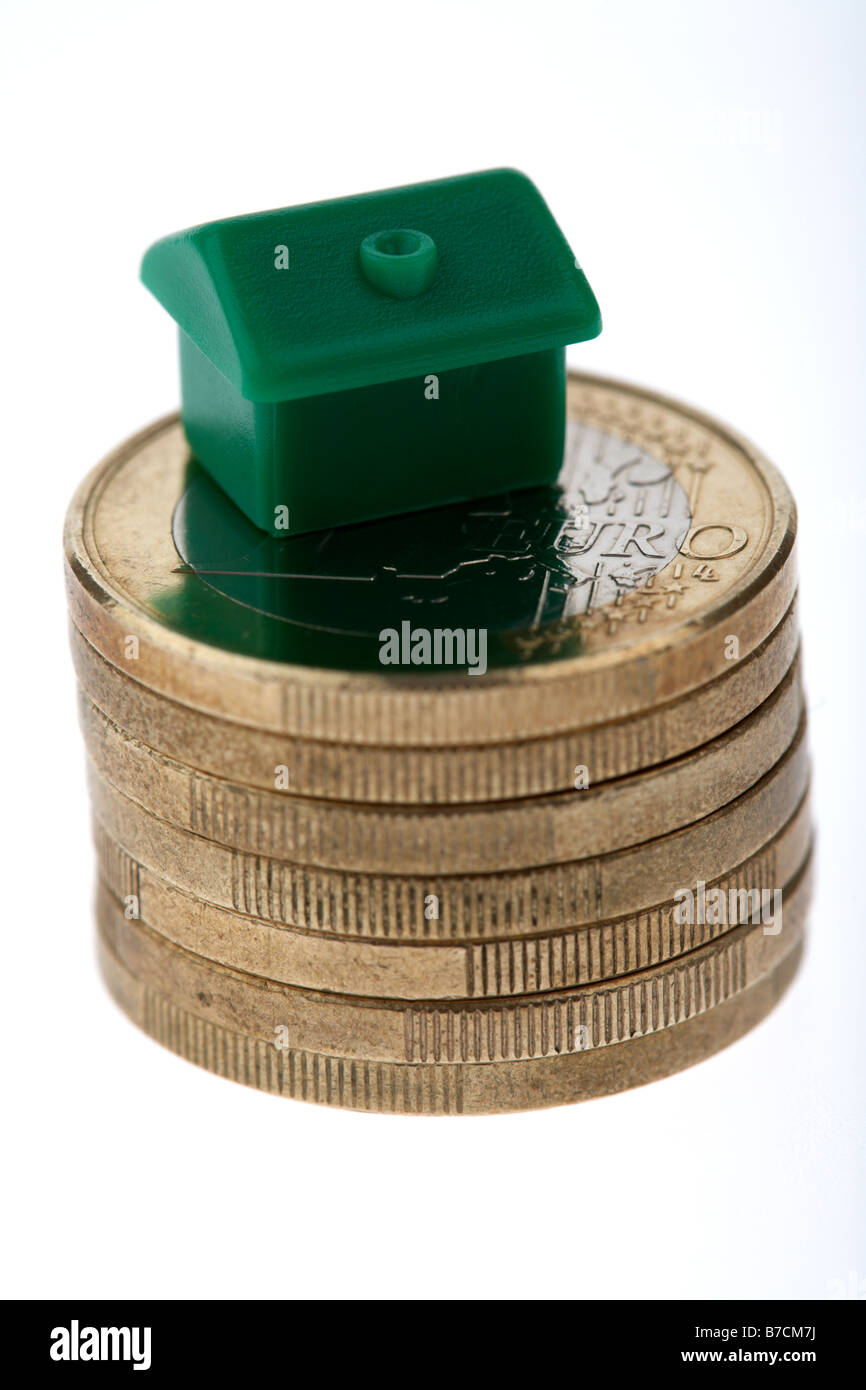 small toy house sitting on top of a pile of used euro coins on white background Stock Photo