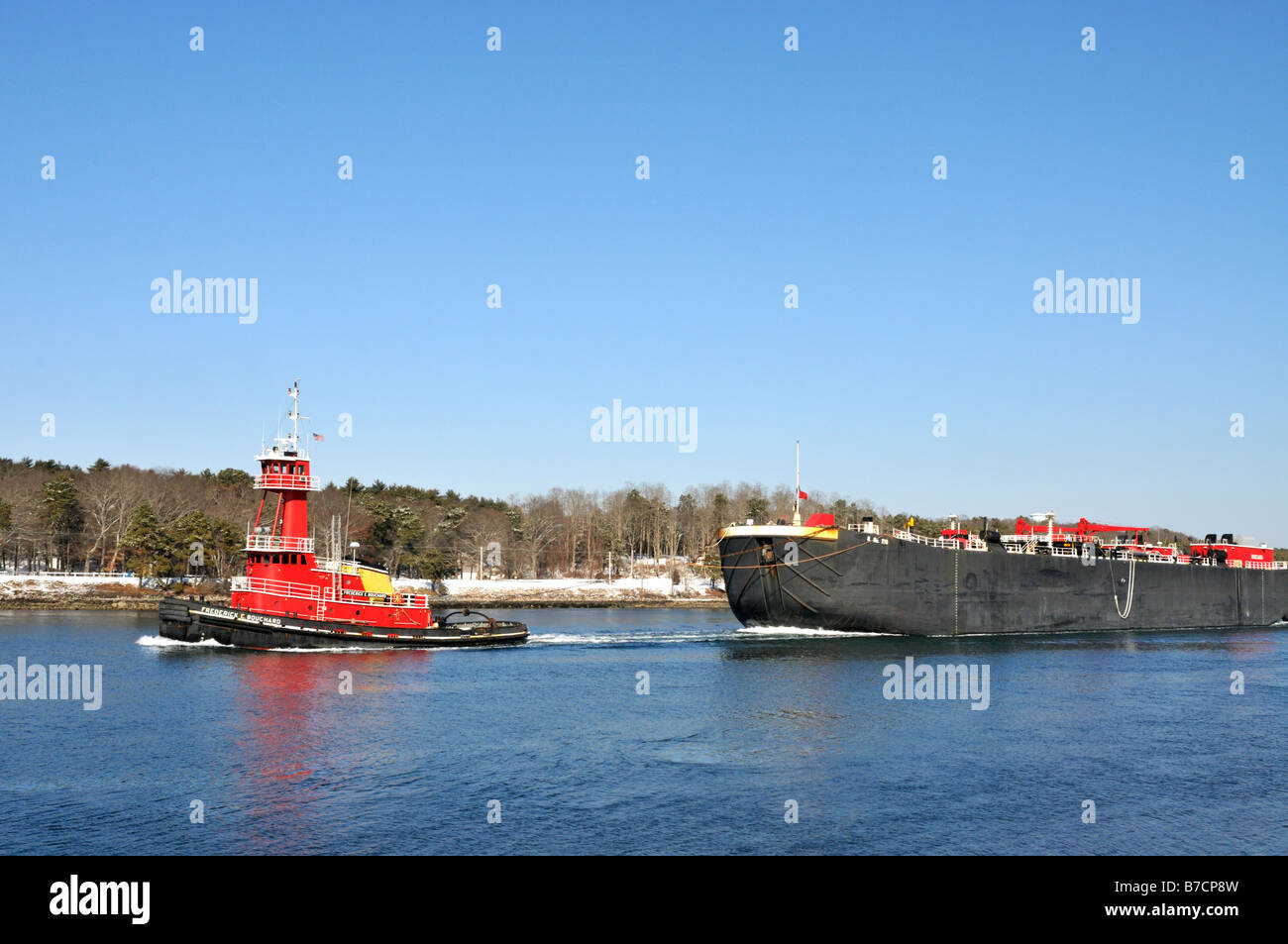 Red tugboat pulling barge through canal Stock Photo