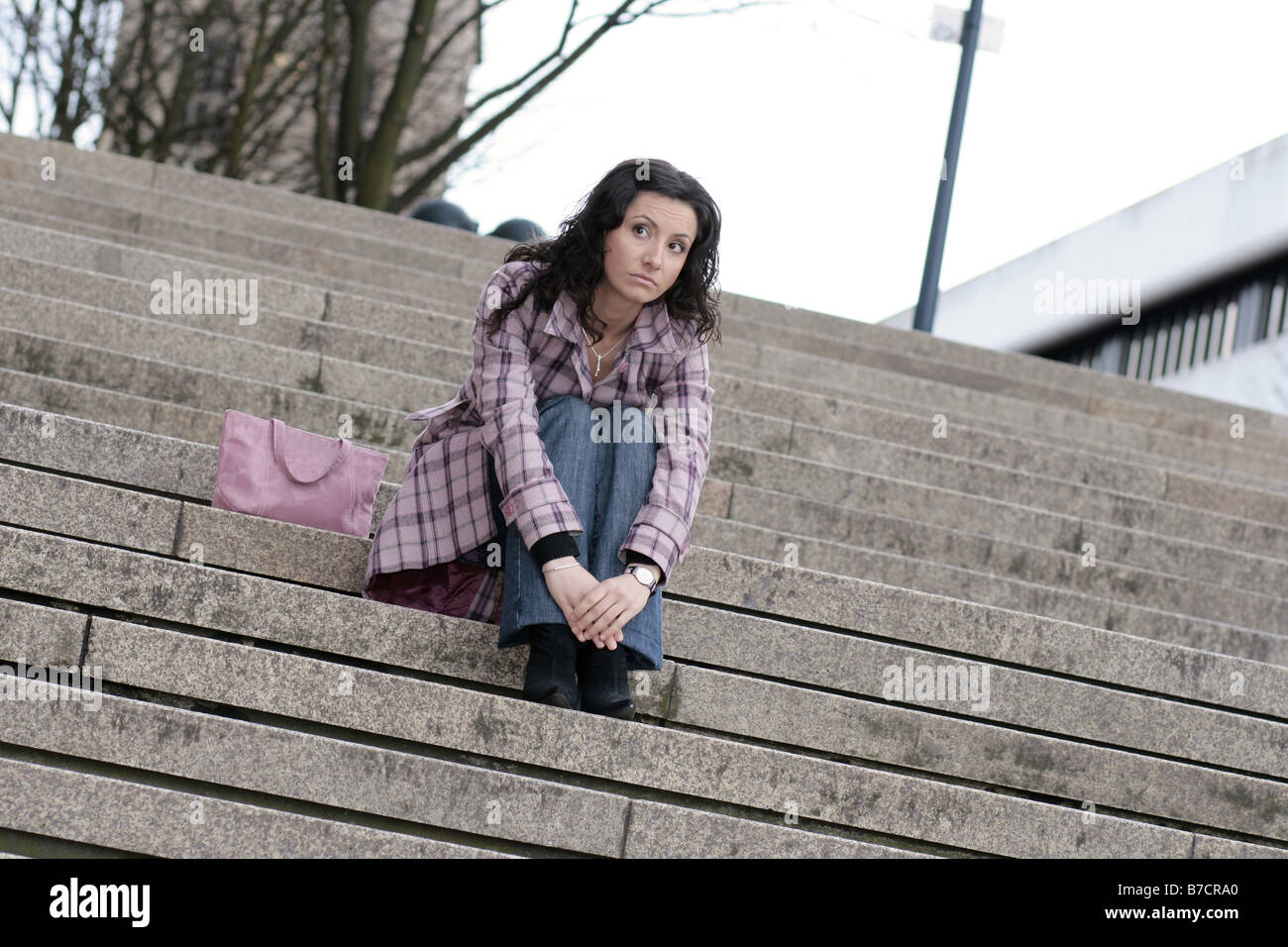 young darkhaired woman sitting on stairs, waiting Stock Photo