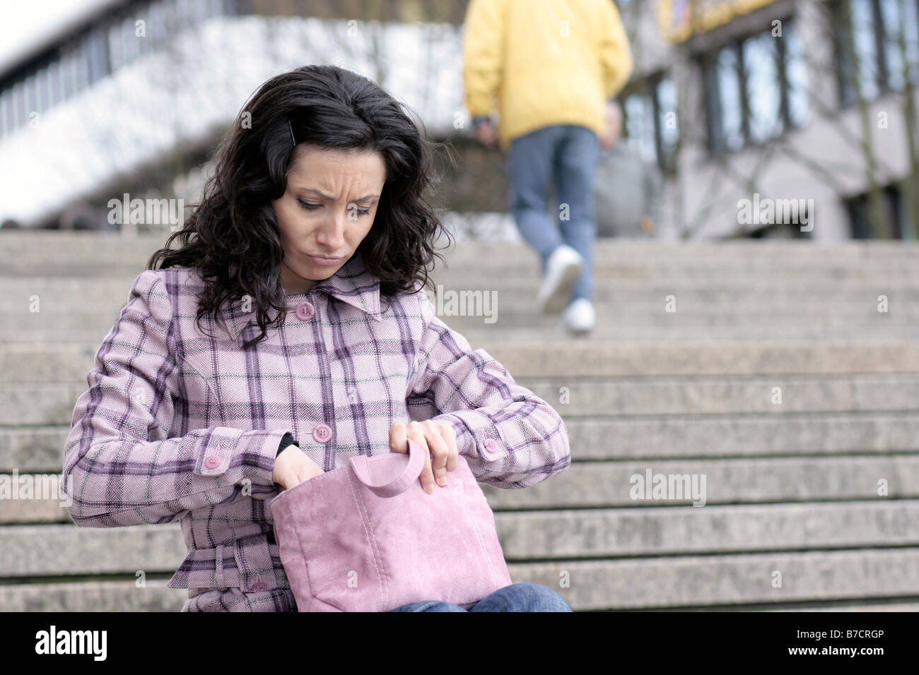 young darkhaired sitting on stairs, looking for something in her handbag Stock Photo