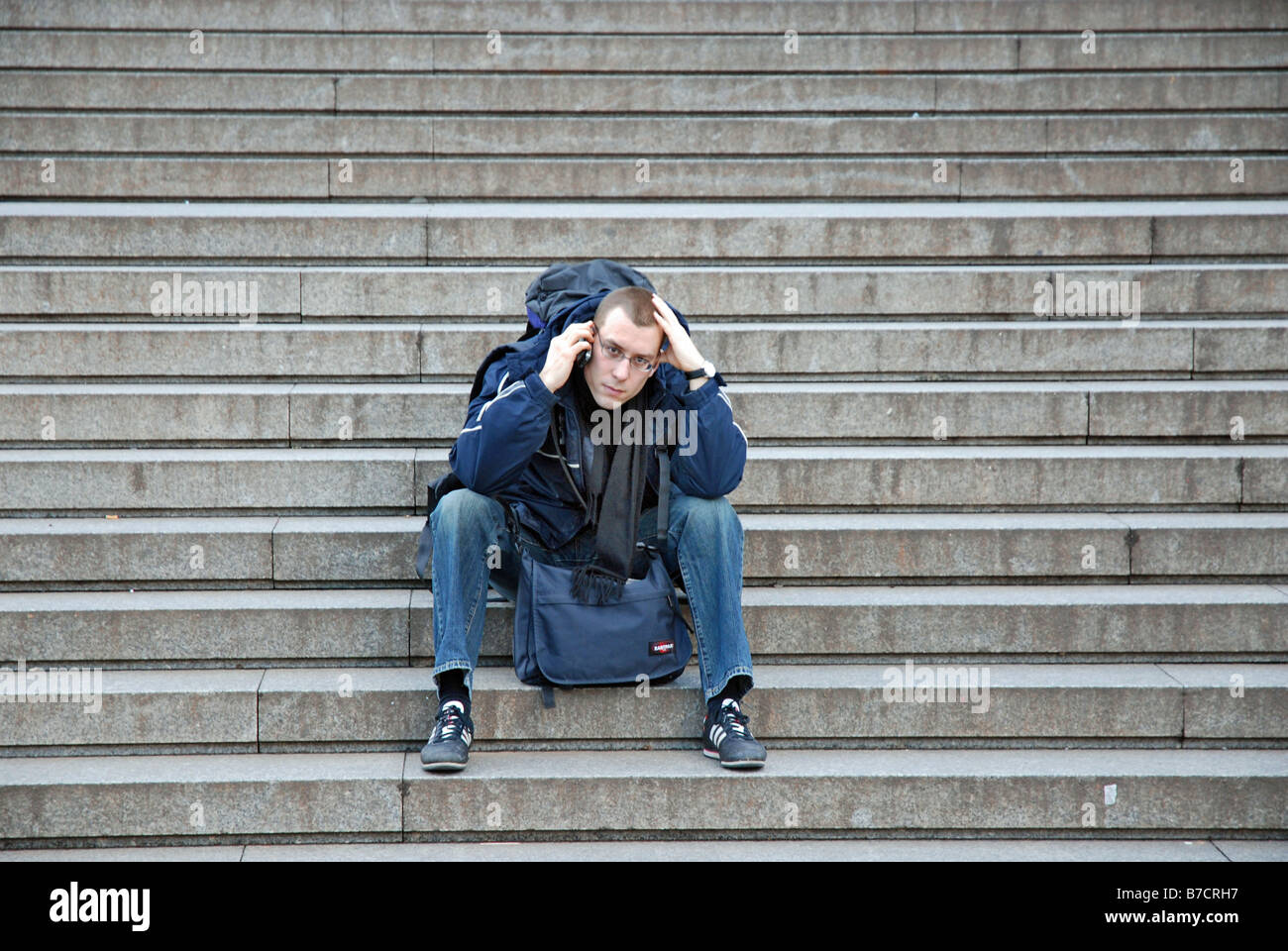 young tourist with mobile phone sitting on stairs, Germany, North Rhine-Westphalia, Koeln Stock Photo