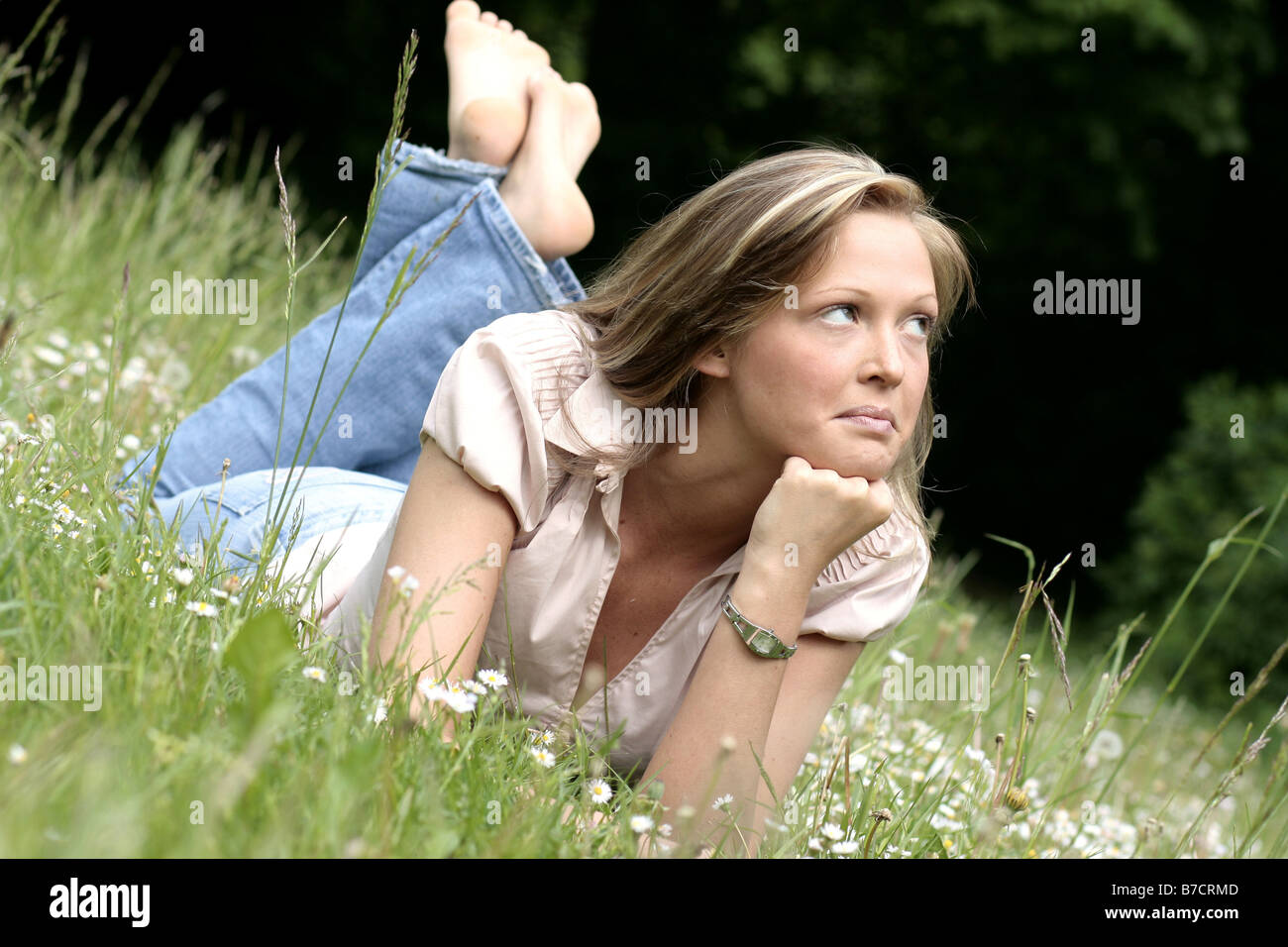 young blond woman lying on a meadow, with her chin on her hand Stock Photo