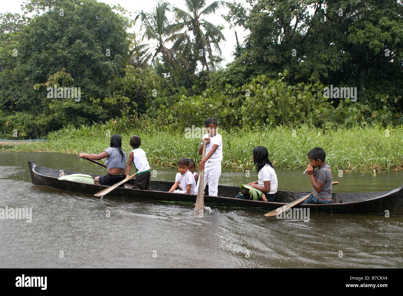 Children in a dugout trying to protect a baby with a palm leaf in heavy rain on Rio San Juan River, Nicaragua, Rio San Juan Stock Photo