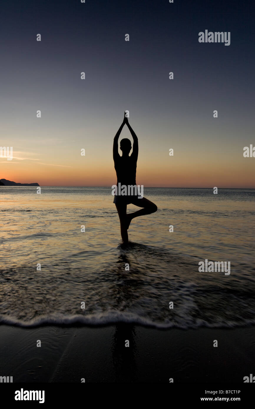 Silhouette of young woman doing yoga at the beach during sunset in
