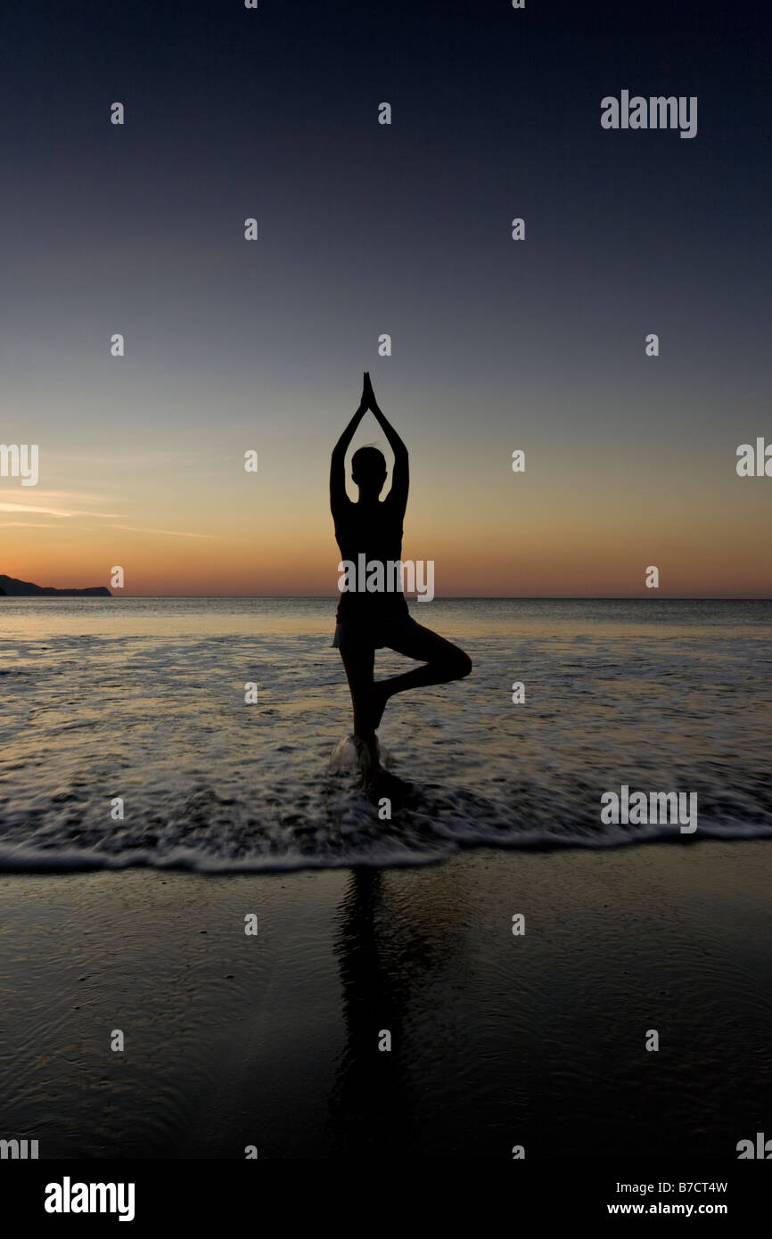 Silhouette of young woman doing yoga at the beach during sunset in ...